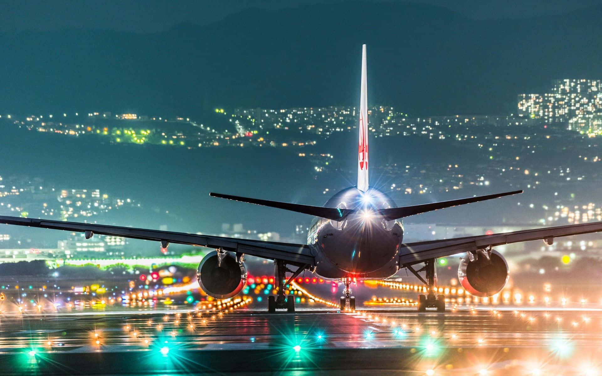 飛機 桌布 壁紙 — 一架大型飛機在夜間停在濕滑的跑道上，背景中城市燈光閃爍。