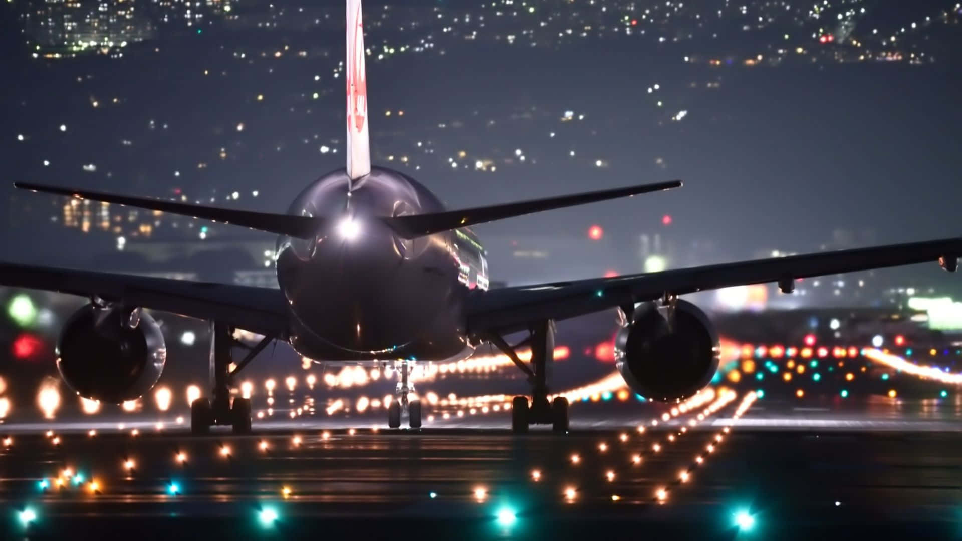飛機 桌布 壁紙 — 一架大型飛機在夜間停在跑道上，背景中城市燈光閃爍。