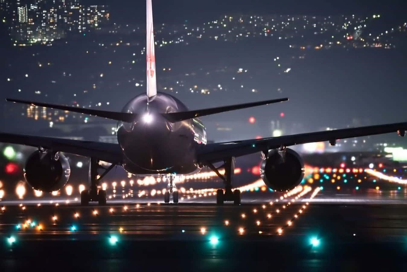 飛機 桌布 壁紙 — 一架大型飛機在夜間停在跑道上，背景中城市燈光閃爍。