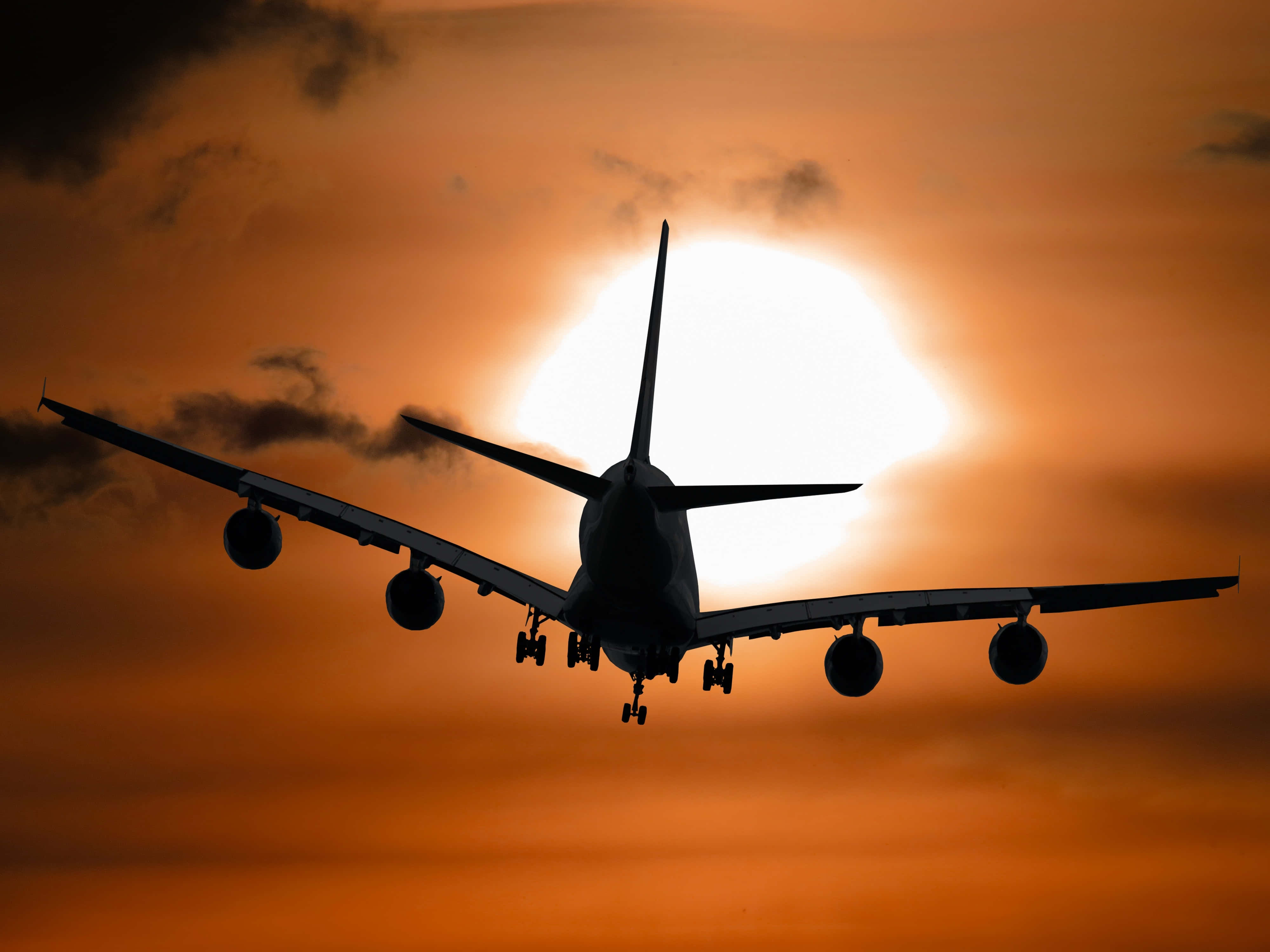 Flight 桌布 壁紙 — 一架大型飛機在帶有雲朵的橙色日落天空襯托下形成剪影。