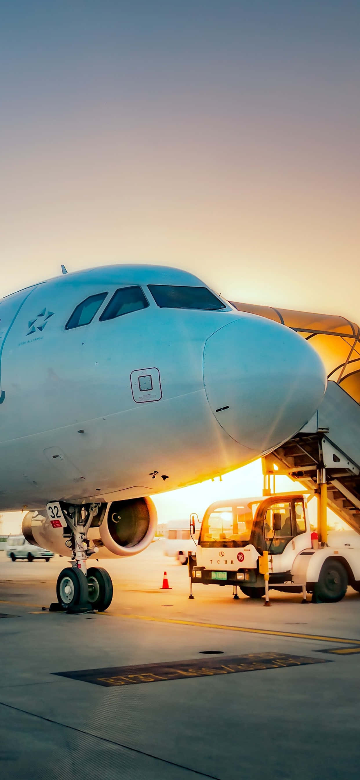 Plane 桌布 壁紙 — 一架大型飛機在日落時停在停機坪上，附近有登機橋和地面車輛。