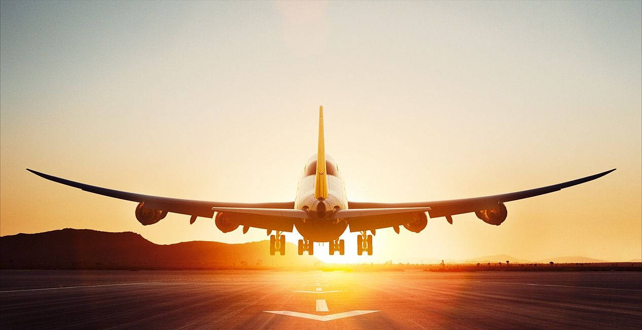飛機 桌布 壁紙 — 一架大型飛機在日落時分在跑道上滑行，背後閃耀著金色的光芒。