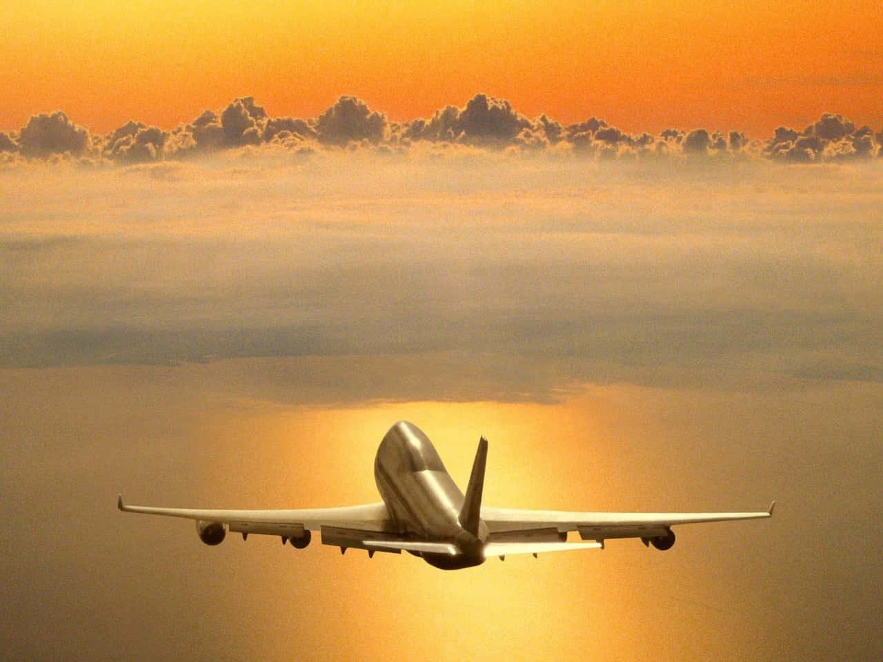 飛機 桌布 壁紙 — 一架大型飛機在日落時分翱翔於金色雲層之上，溫暖的橙色和黃色色調沐浴著天空。