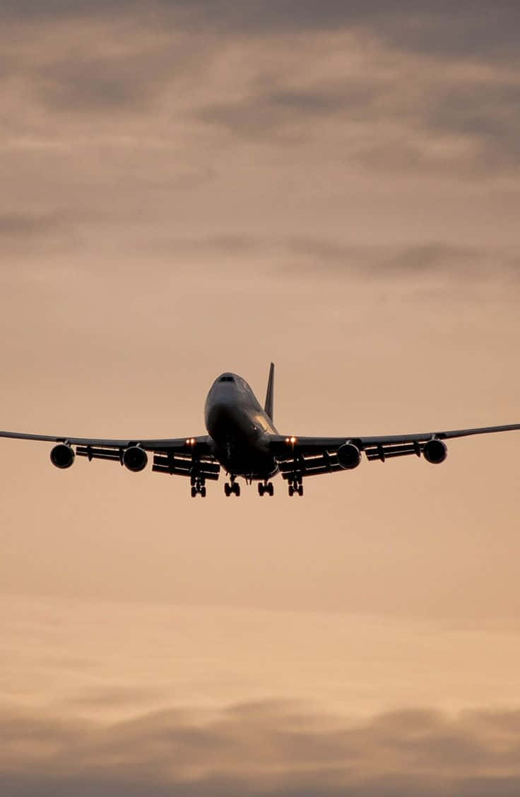 747 Airplane 桌布 壁紙 — 一架大型飛機在柔和橙粉色的日落天空與散落的雲朵中下降。
