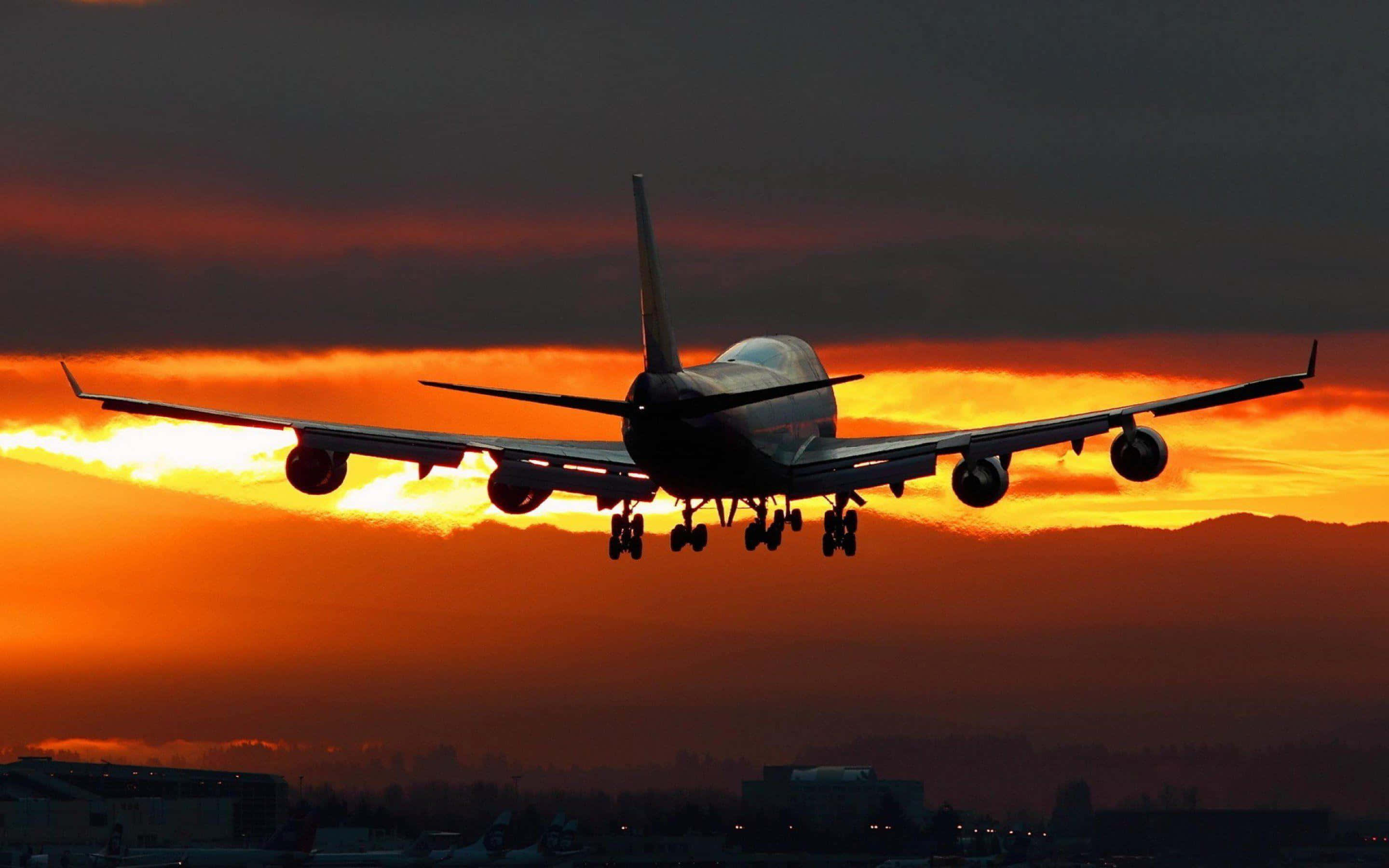 飛機 桌布 壁紙 — 一架大型飛機在火紅橙色夕陽天空的襯托下呈現剪影，正在下降準備著陸。