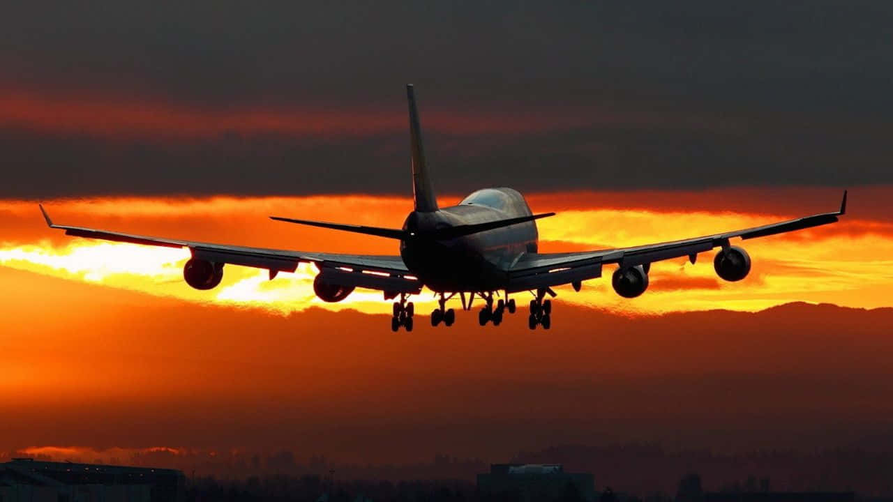 720p Plane 桌布 壁紙 — 一架大型飛機在熾熱的橙紅色日落天空襯托下，呈現剪影，正下降準備著陸。