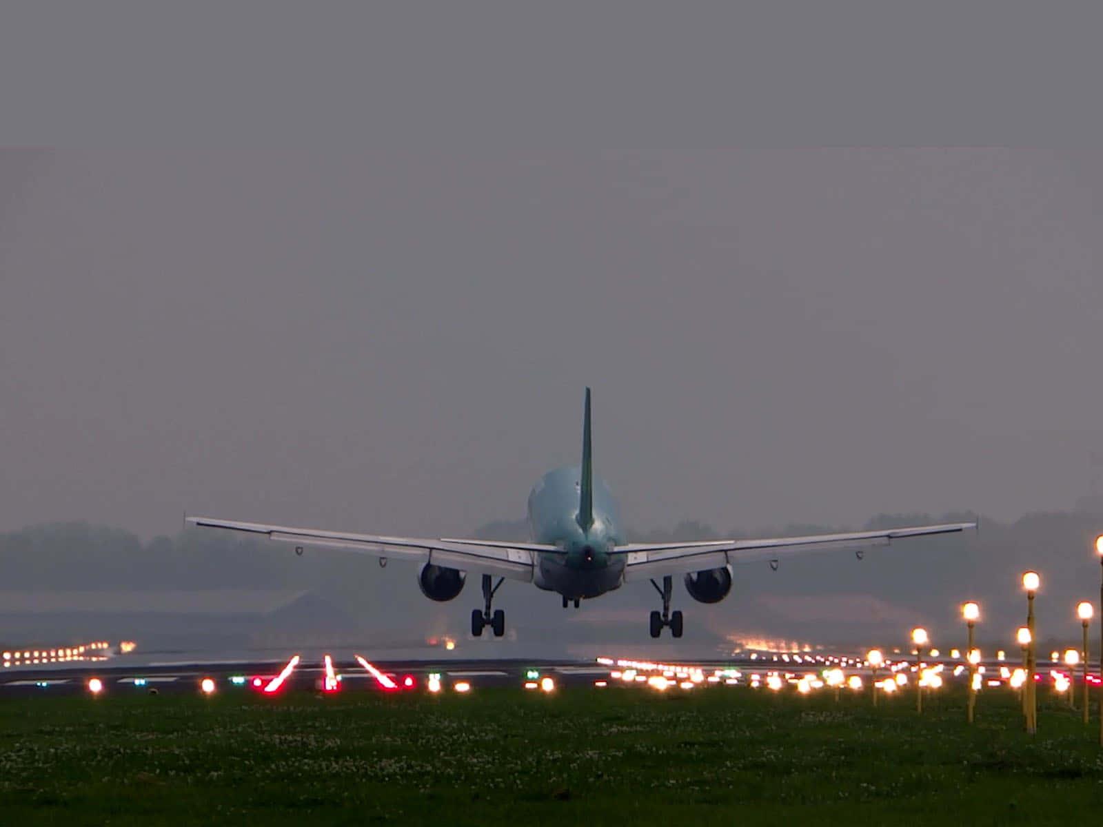 Airport 桌布 壁紙 — 一架大型飛機在黃昏時分降落到跑道，停機坪和草地上排列著發光的燈光。