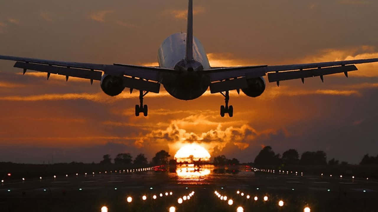 720p Plane 桌布 壁紙 — 一架大型飛機正在下降至跑道，太陽在其後方落下，將溫暖的橙色光線投射在雲層和跑道燈上。