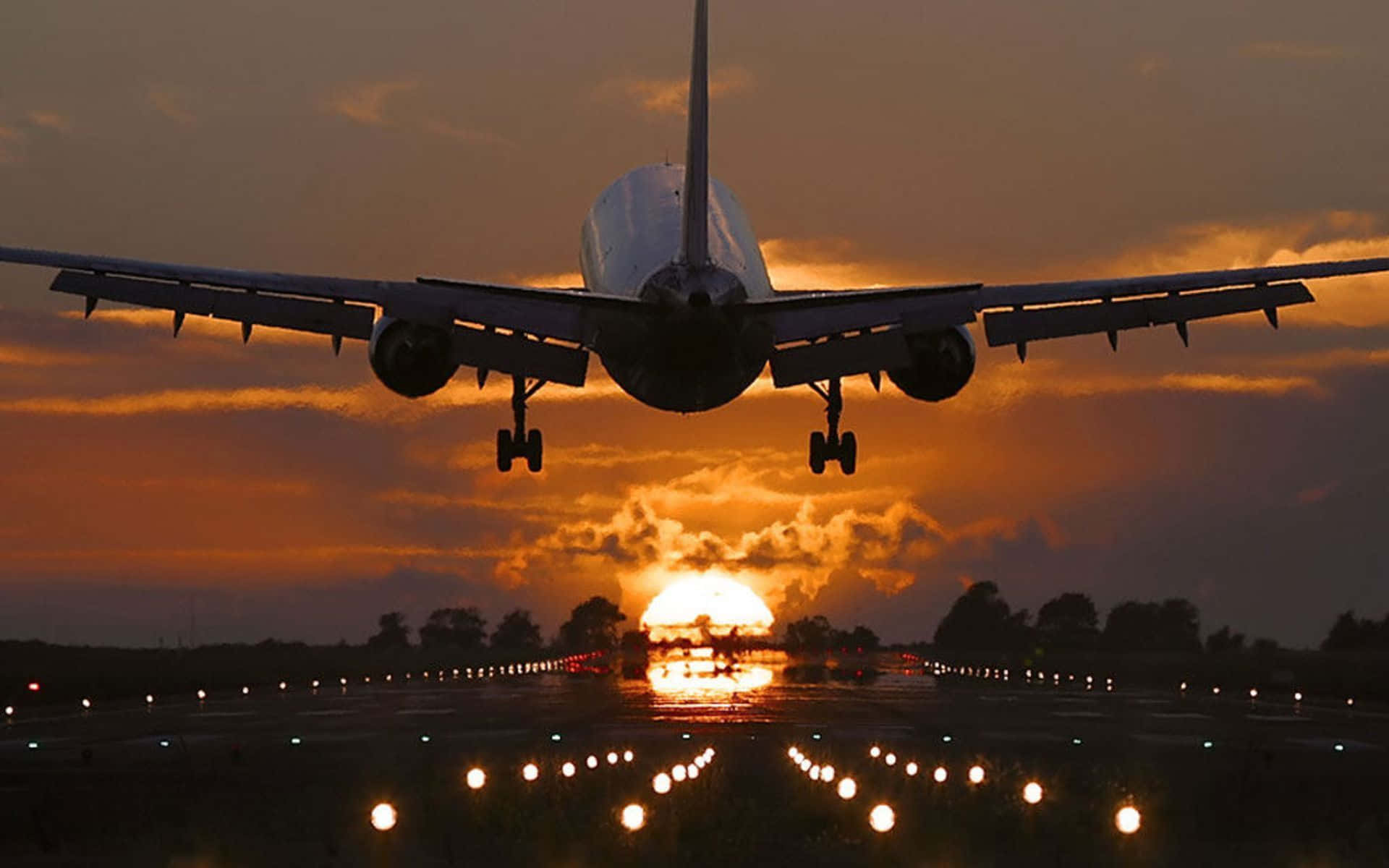 Plane Desktop 桌布 壁紙 — 一架大型飛機正在下降至跑道，太陽在其後方落下，將金色光芒灑在雲層和跑道燈上。