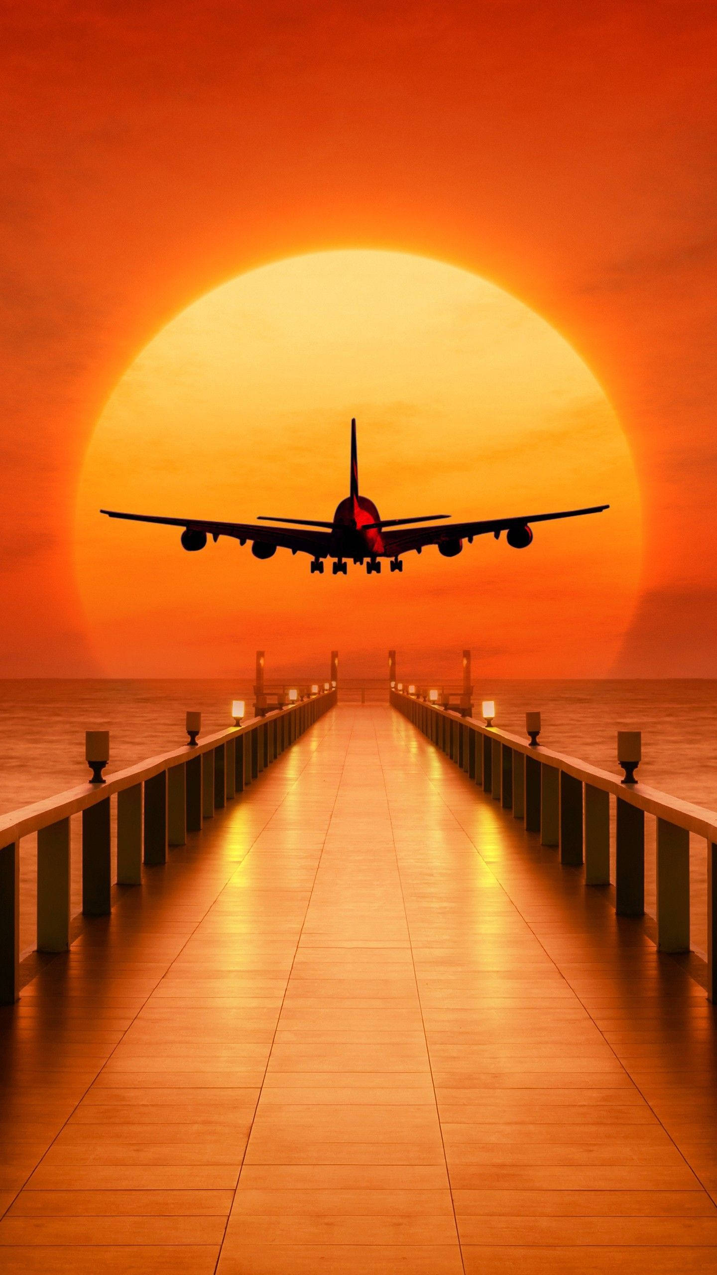 4K 飛機壁紙 桌布 壁紙 — 一架大型飛機的剪影在日落時分向碼頭下降，背後有一個巨大的橙色太陽。
