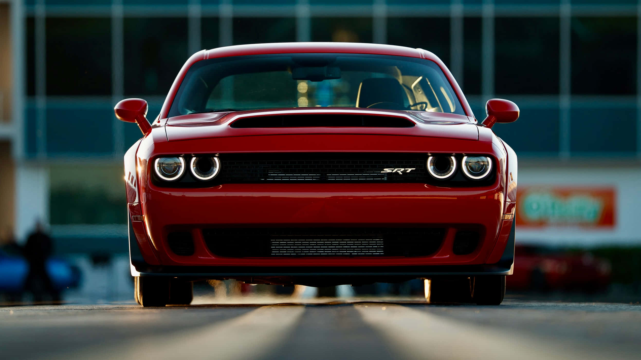 Dodge 桌布 壁紙 — 一架大膽的紅色Dodge Challenger SRT正面朝前，帶有發光的圓形頭燈，背景是現代玻璃建築。