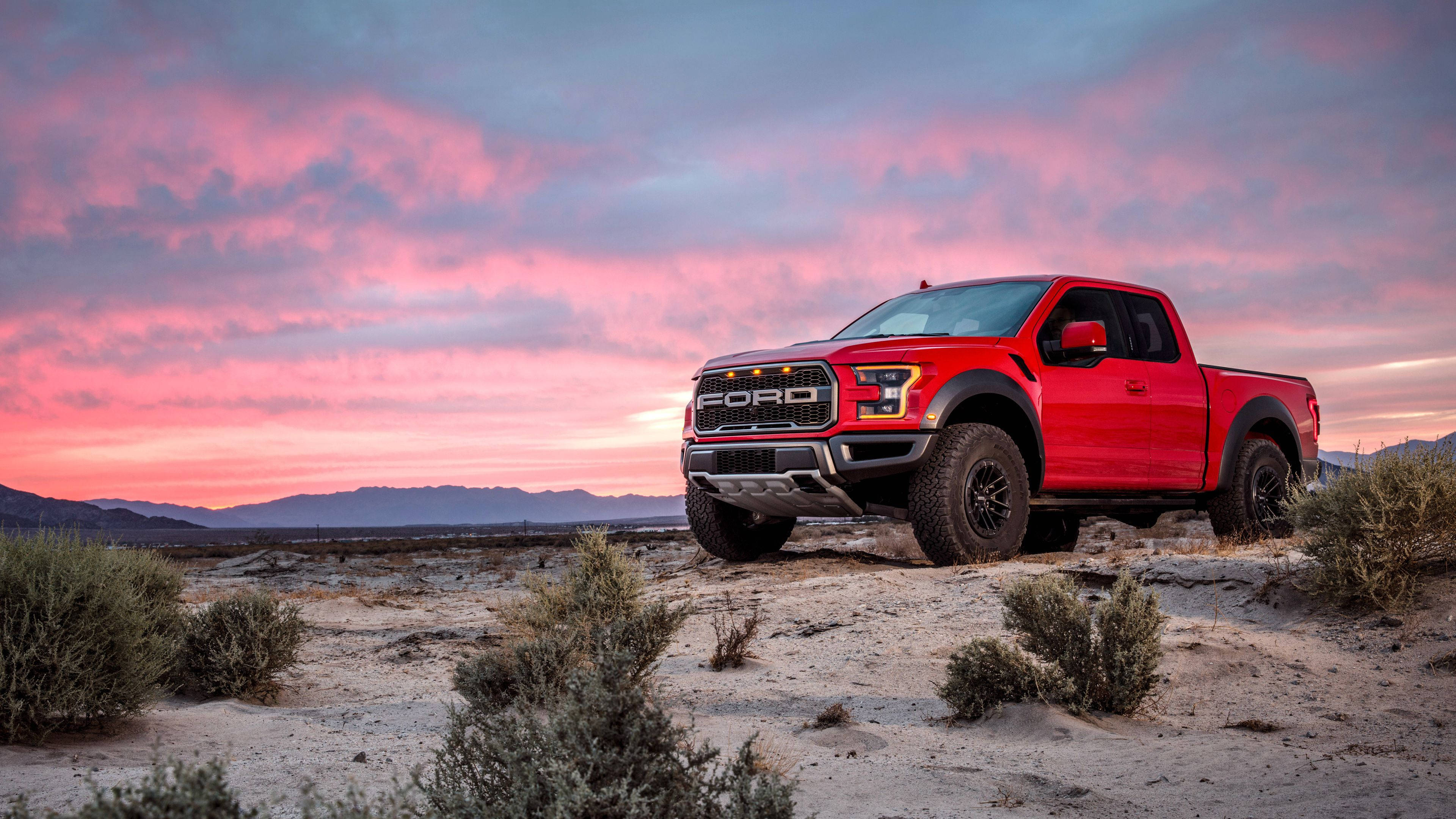 Raptor 桌布 壁紙 — 一架大膽的紅色Ford F-150 Raptor在戲劇性的粉紅和紫色日落天空下，屹立於沙漠山脊上。