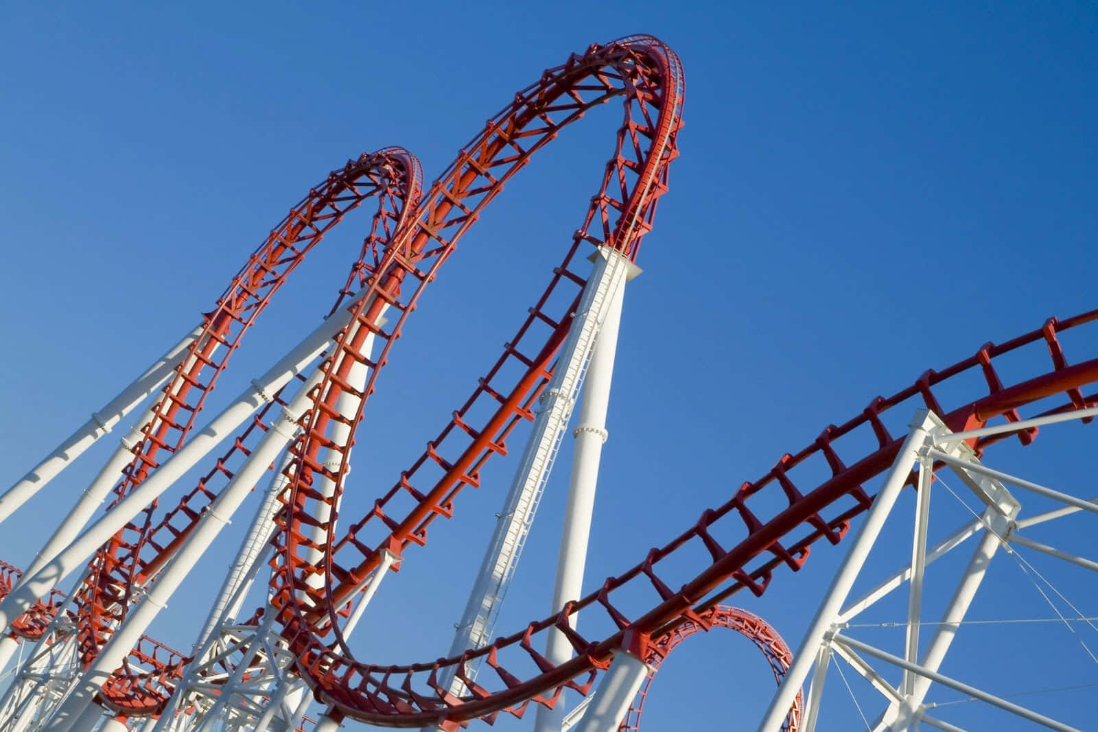 Roller Coaster 桌布 壁紙 — 一架大膽的紅色雲霄飛車在晴朗的藍天下扭轉和迴圈，構成一個刺激的遊樂園場景。
