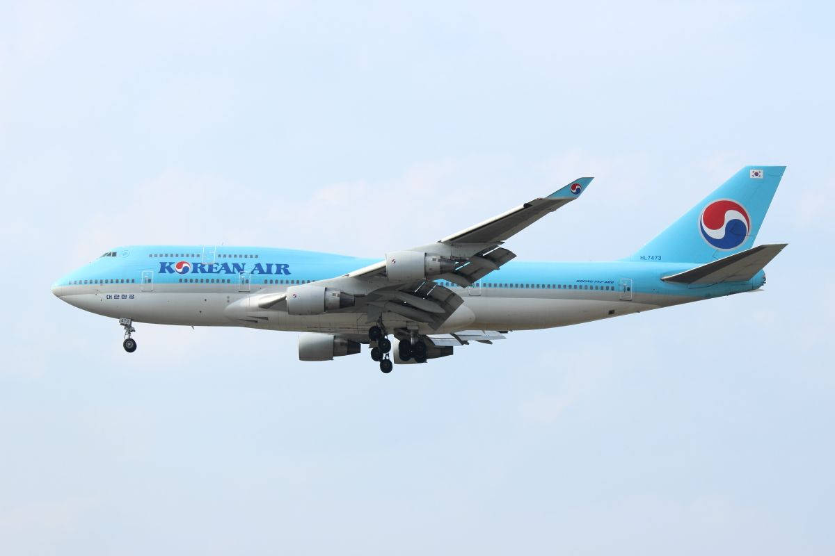 飛機 桌布 壁紙 — 一架大韓航空波音747以淺藍色塗裝，在日間飛行中優雅地傾斜，襯著蒼白的天空。