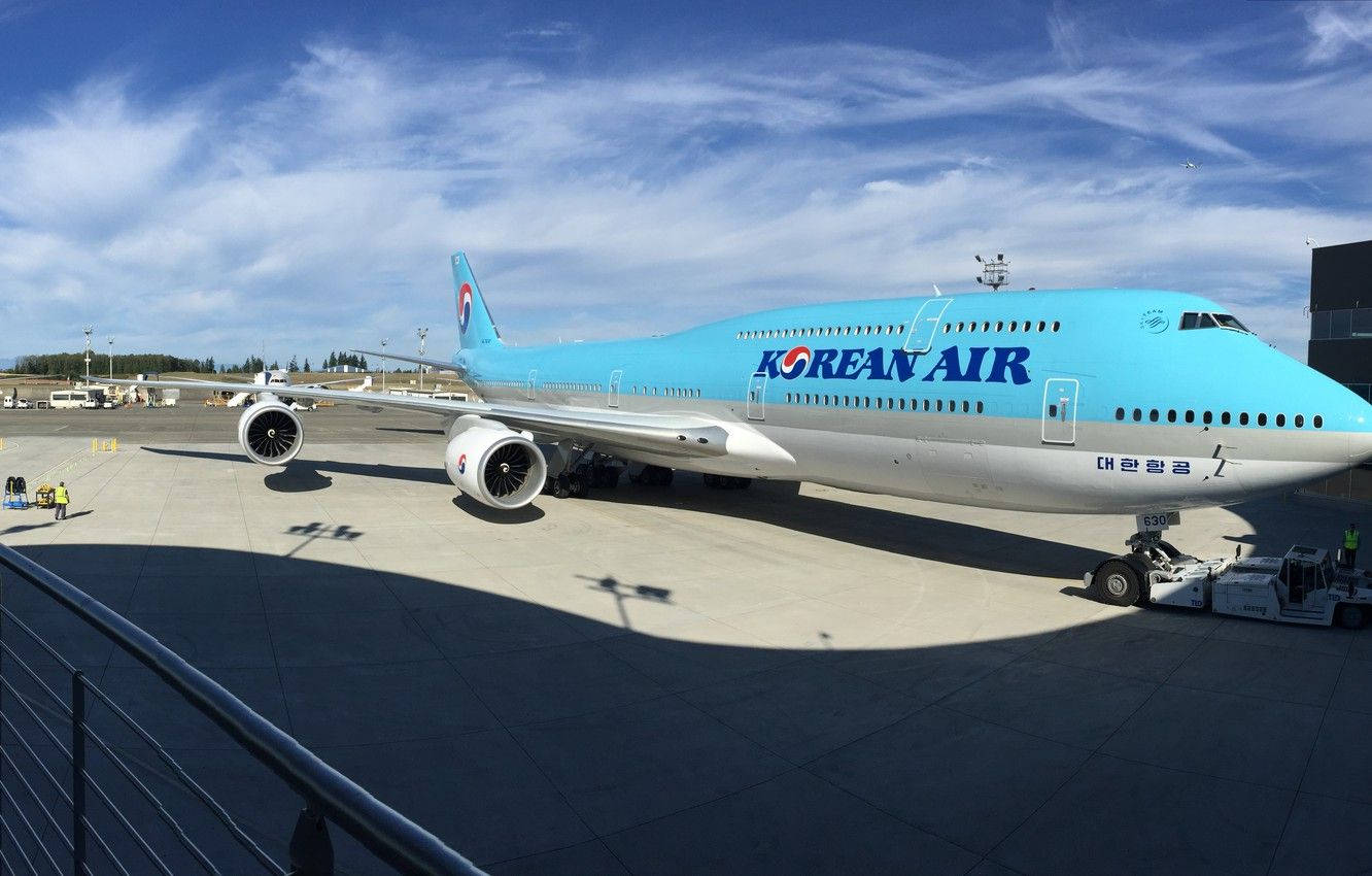 飛機 桌布 壁紙 — 一架大韓航空波音747停泊在陽光普照的機場停機坪上，天空湛藍，白雲點綴。