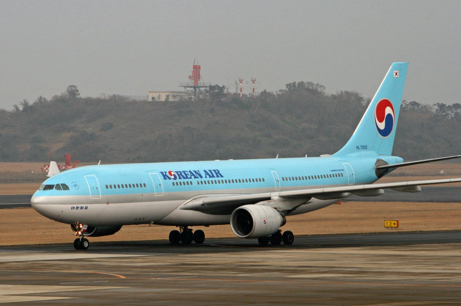 風景 桌布 壁紙 — 一架大韓航空空中巴士A330在跑道上滑行，背景有朦朧的山丘和通訊塔。