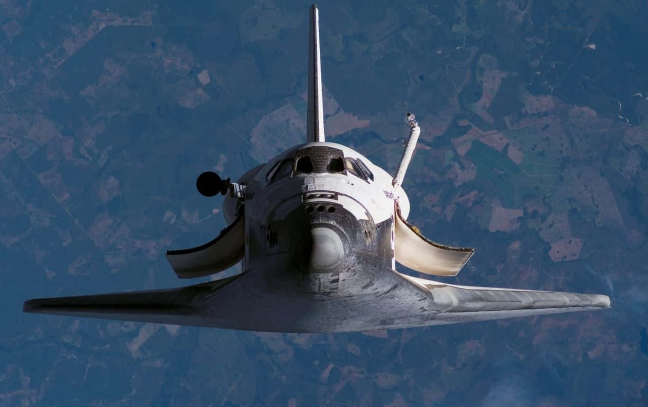 space shuttle 桌布 壁紙 — 一架太空梭在地球上空翱翔，下方是藍色和綠色的陸地拼湊而成的圖案。
