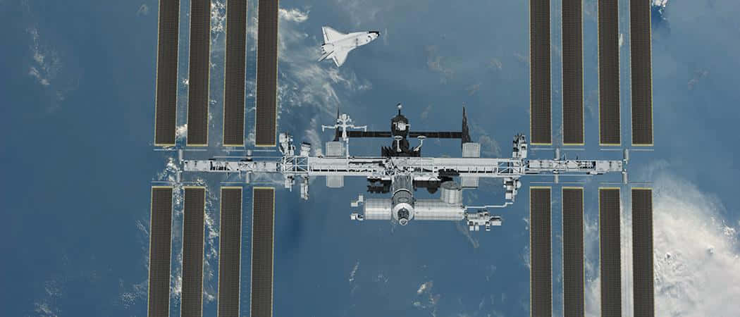 International Space Station 桌布 壁紙 — 一架太空梭正在地球的藍色海洋和白色雲層上方接近國際太空站。