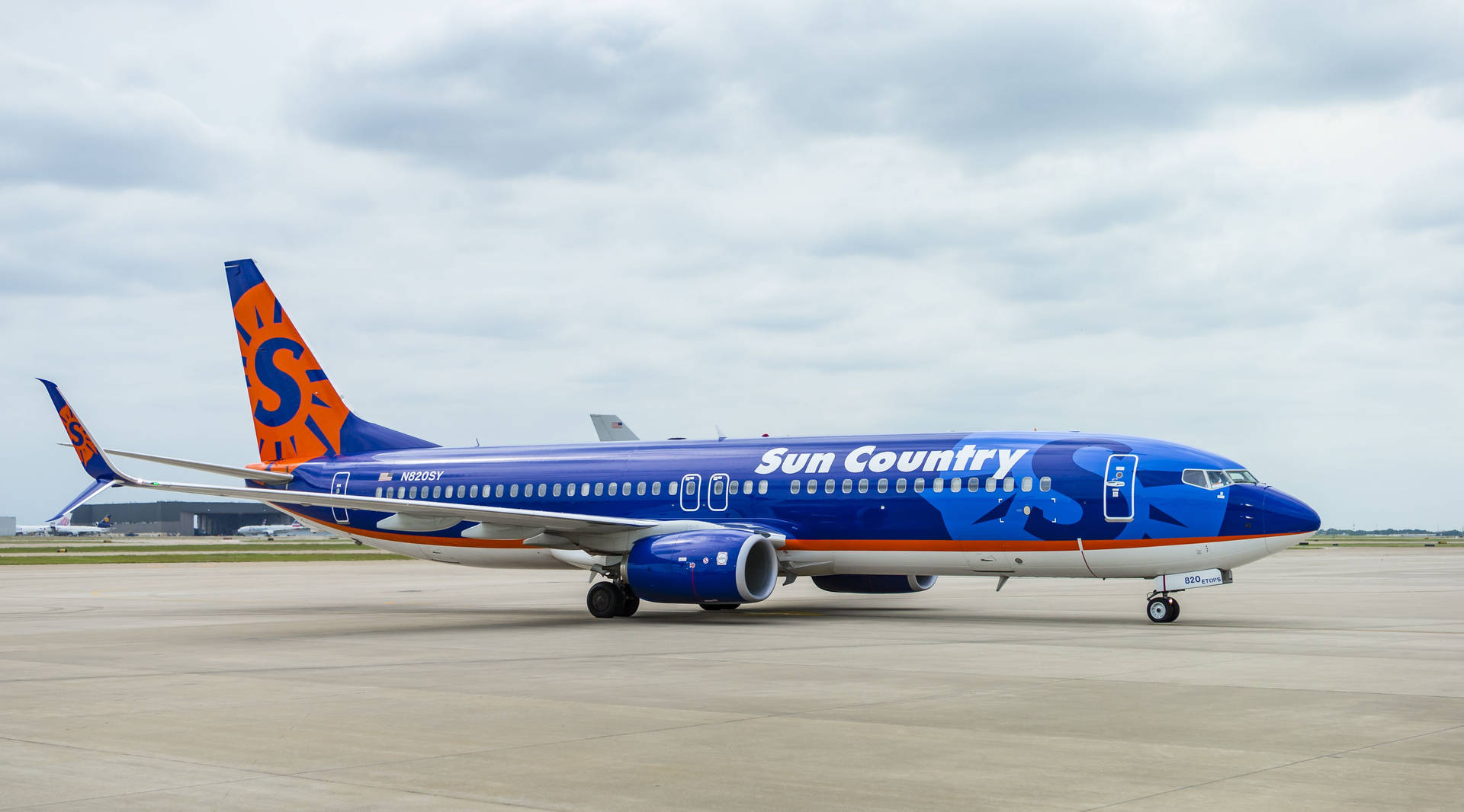  壁紙 — 一架太陽鄉村航空的波音737停放在機場停機坪上，天空多雲，機身塗有鮮豔的藍色和橙色。