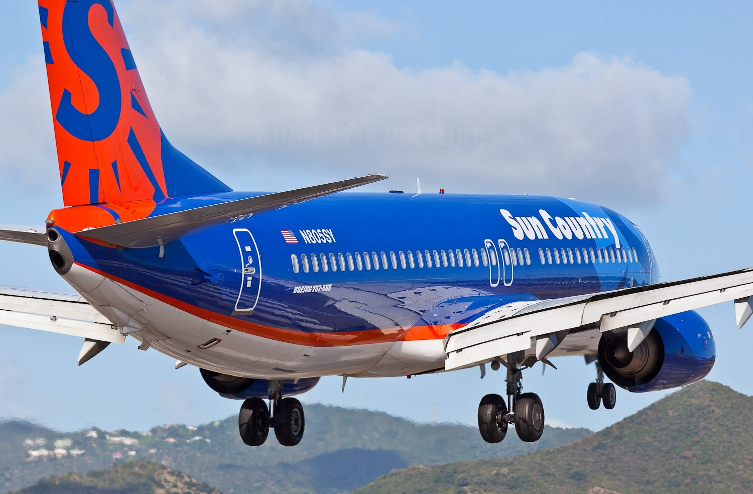 飛機 桌布 壁紙 — 一架太陽鄉村航空的波音737正在降落，起落架放下，背景是綠色山丘和部分多雲的天空。