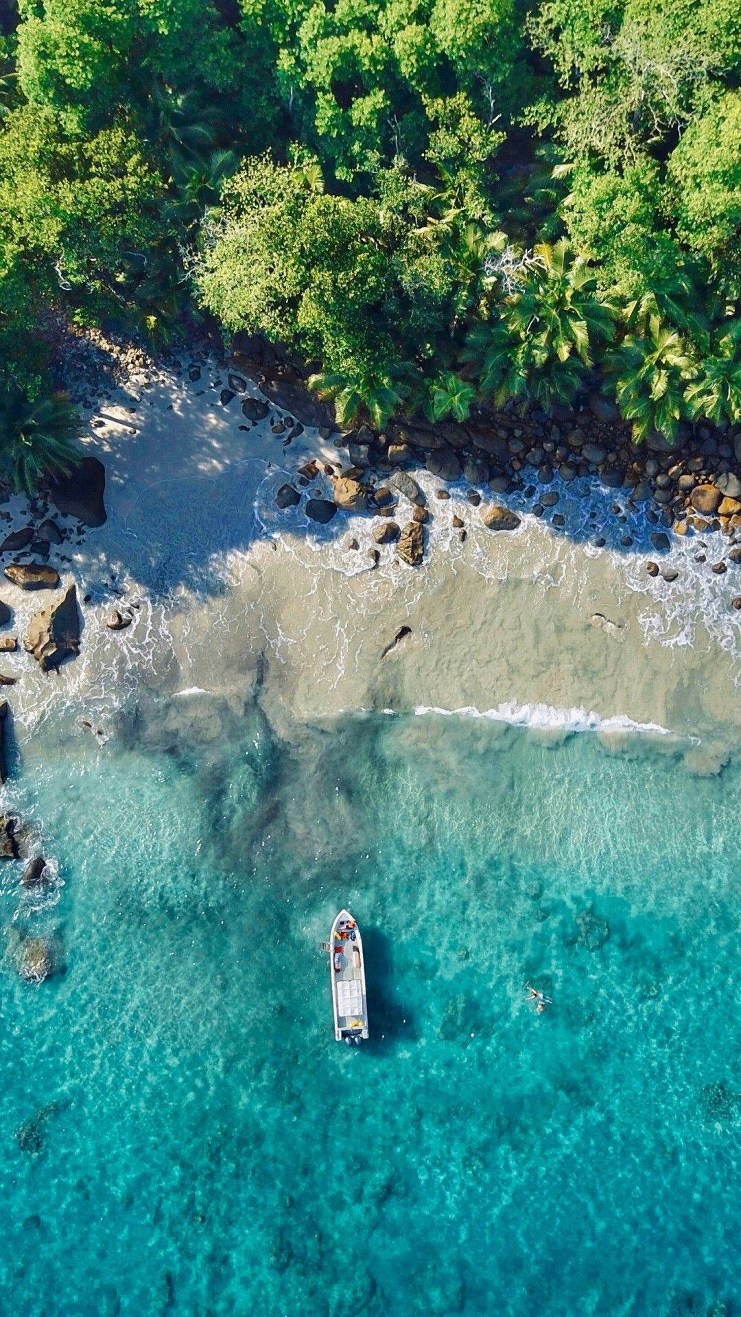 一艘小船漂浮在碧綠的海水中，靠近叢林環繞的岩石海灘。 — 4K 海灘壁紙 壁紙