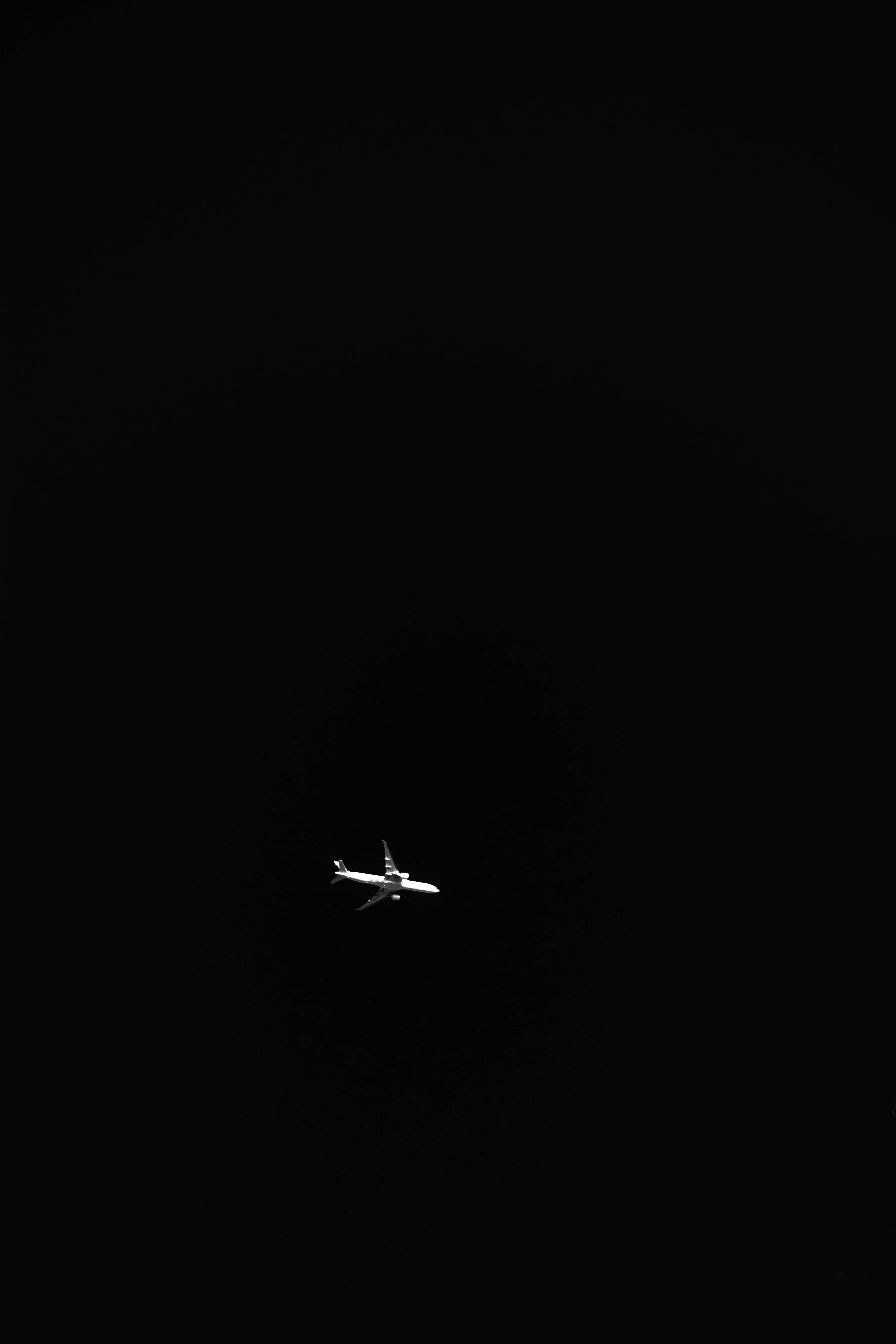 飛機 桌布 壁紙 — 一架孤獨的白色飛機在廣闊漆黑的夜空中滑翔，孤立而寧靜。