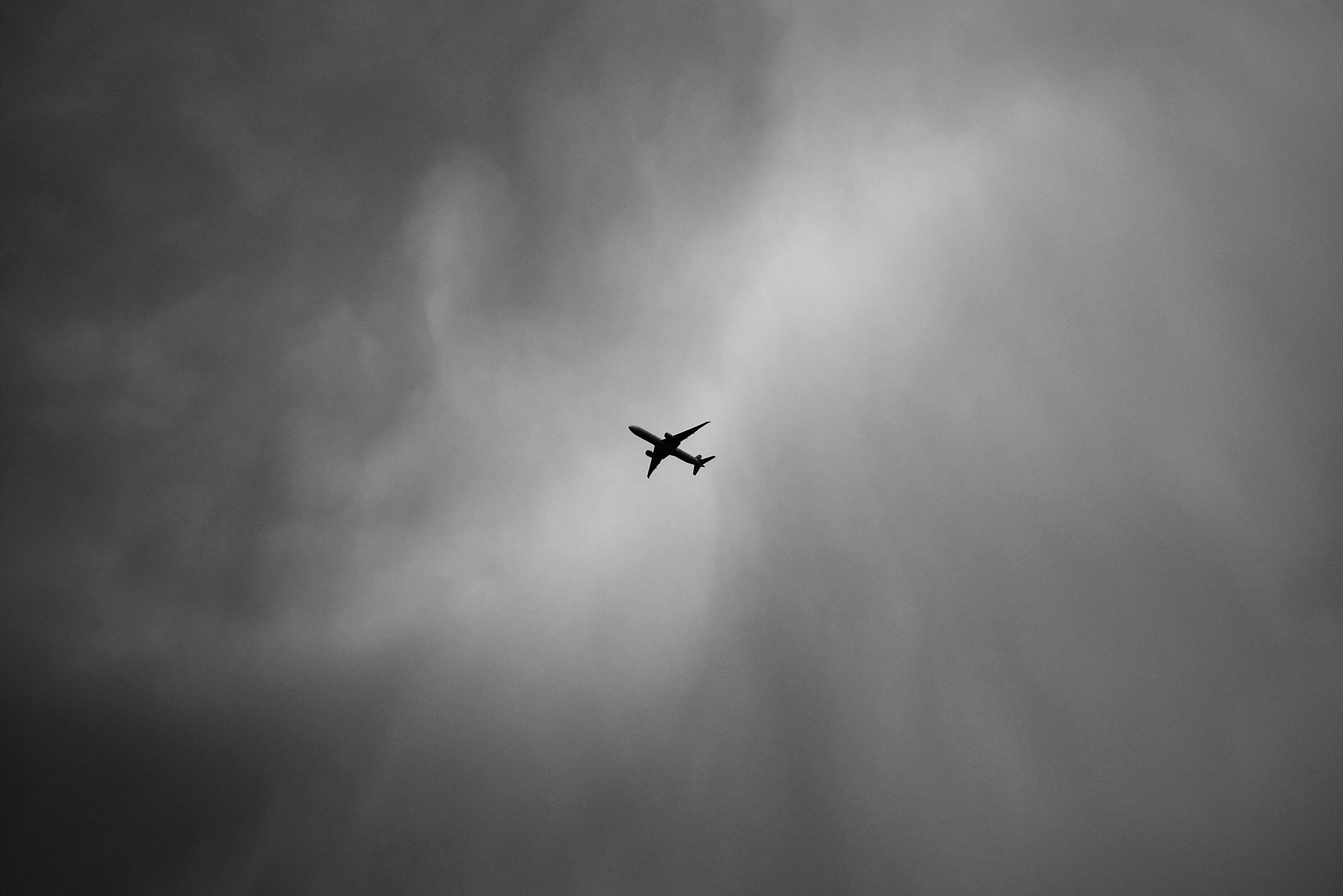飛機 桌布 壁紙 — 一架孤獨的飛機剪影在單色調的戲劇性多雲天空中翱翔。