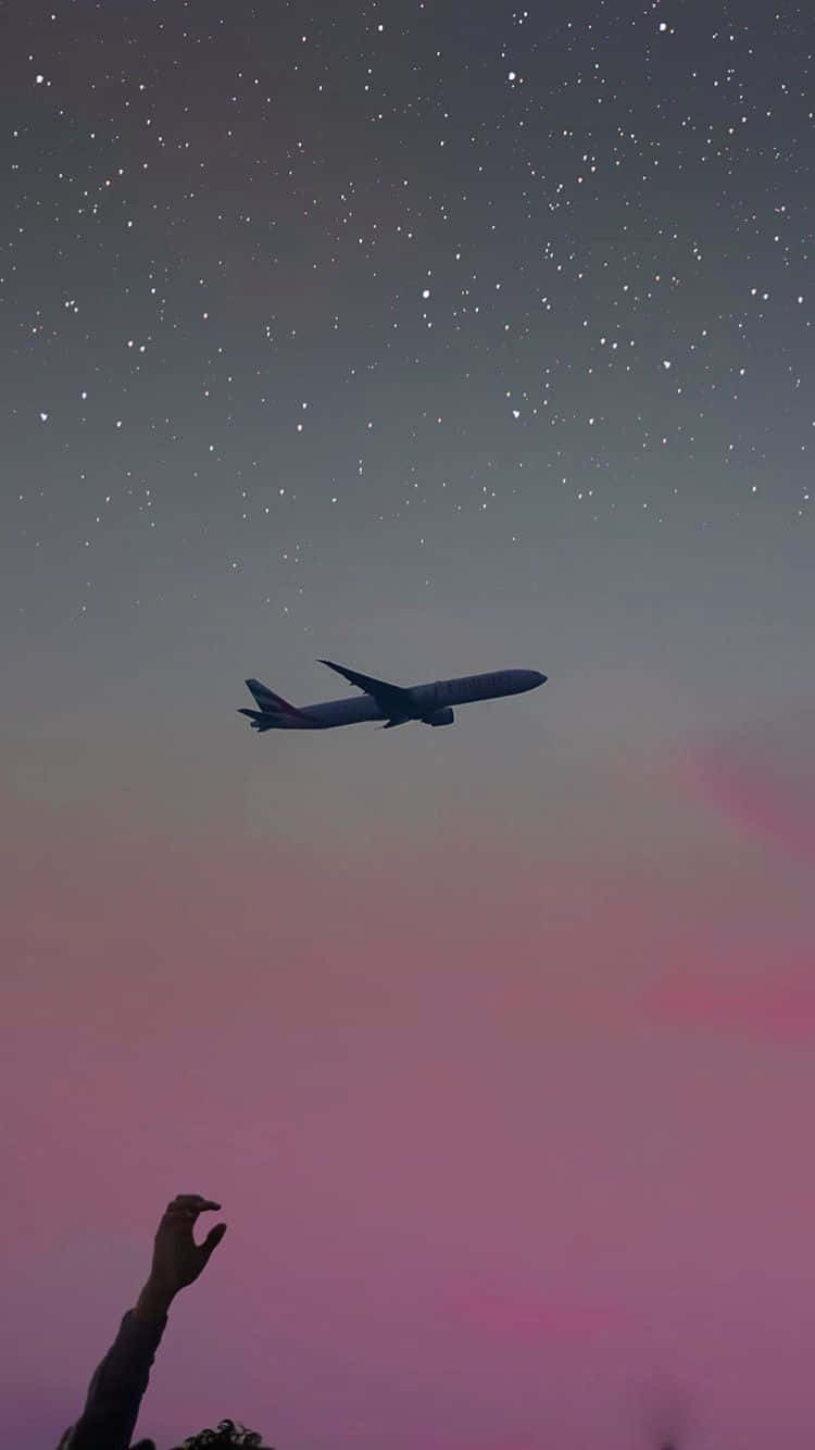 飛機 桌布 壁紙 — 一架孤獨的飛機在佈滿星星的黃昏天空中呈現剪影，帶有粉紅色和紫色色調，下方有一隻手向上伸出。