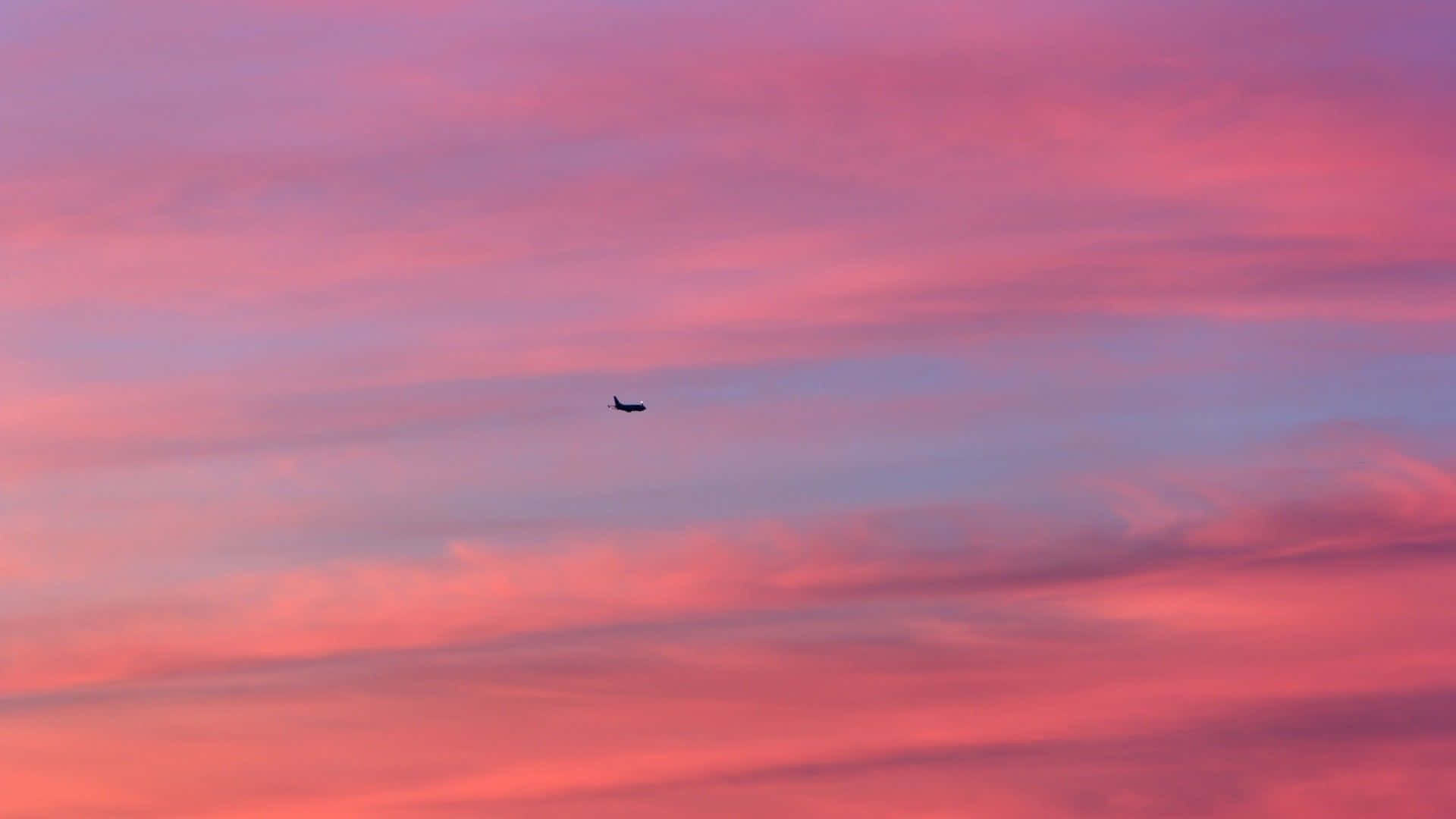 Minimalist Sky 桌布 壁紙 — 一架孤獨的飛機在充滿活力的粉紅色和紫色日落天空與條紋雲的襯托下形成剪影。