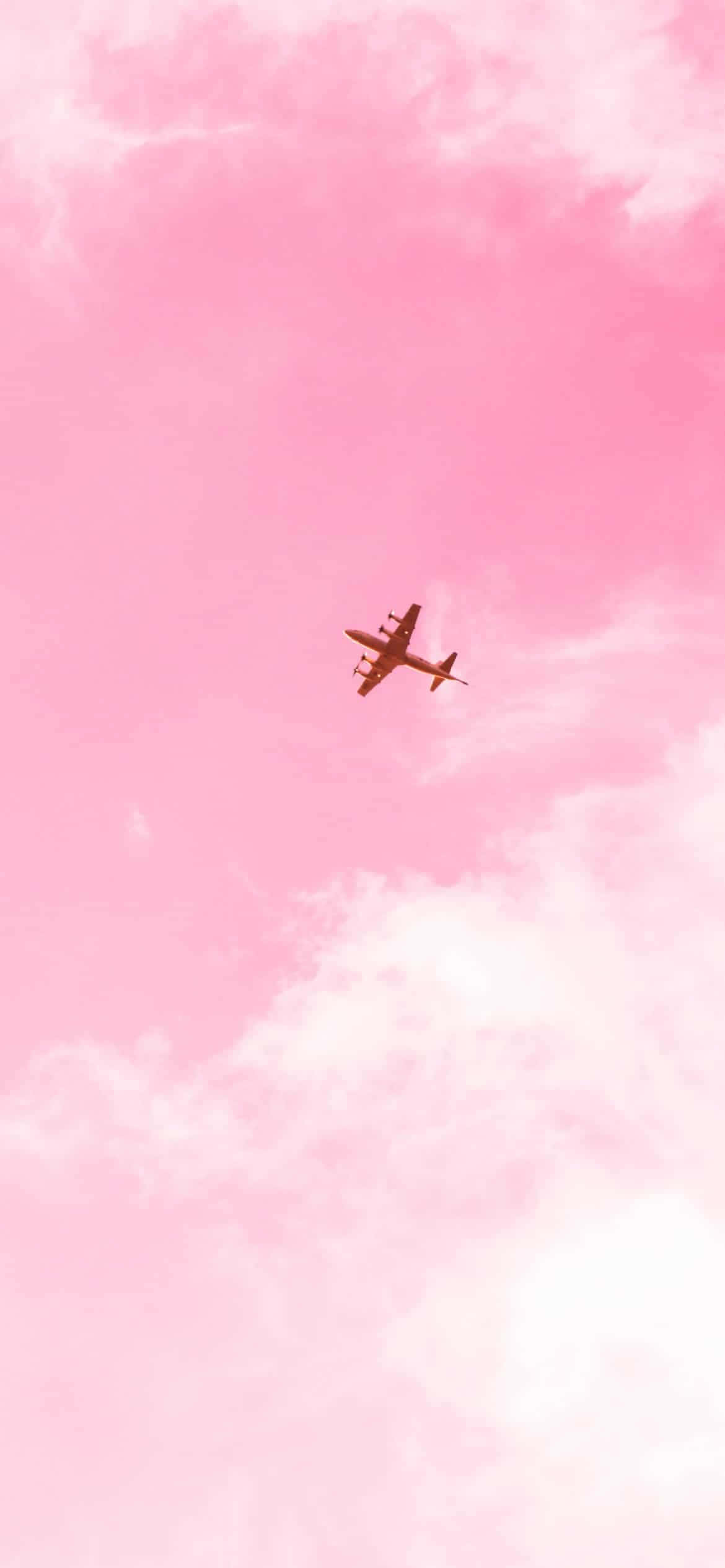 Pink Plane 桌布 壁紙 — 一架孤獨的飛機在夢幻般的粉紅色天空中翱翔，點綴著柔軟的白雲。