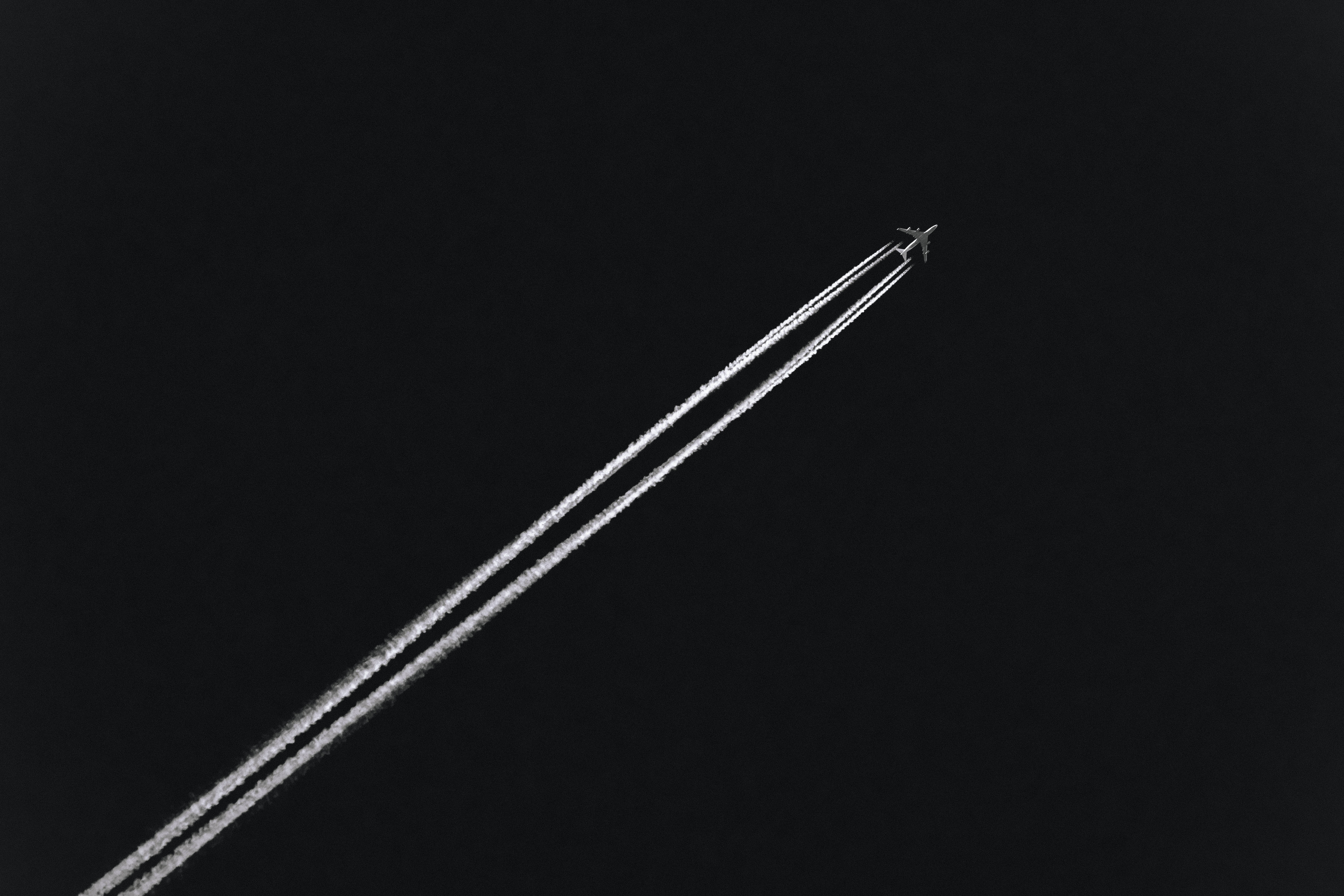 飛機 桌布 壁紙 — 一架孤獨的飛機在廣闊的黑暗夜空中留下兩條平行的凝結尾跡。