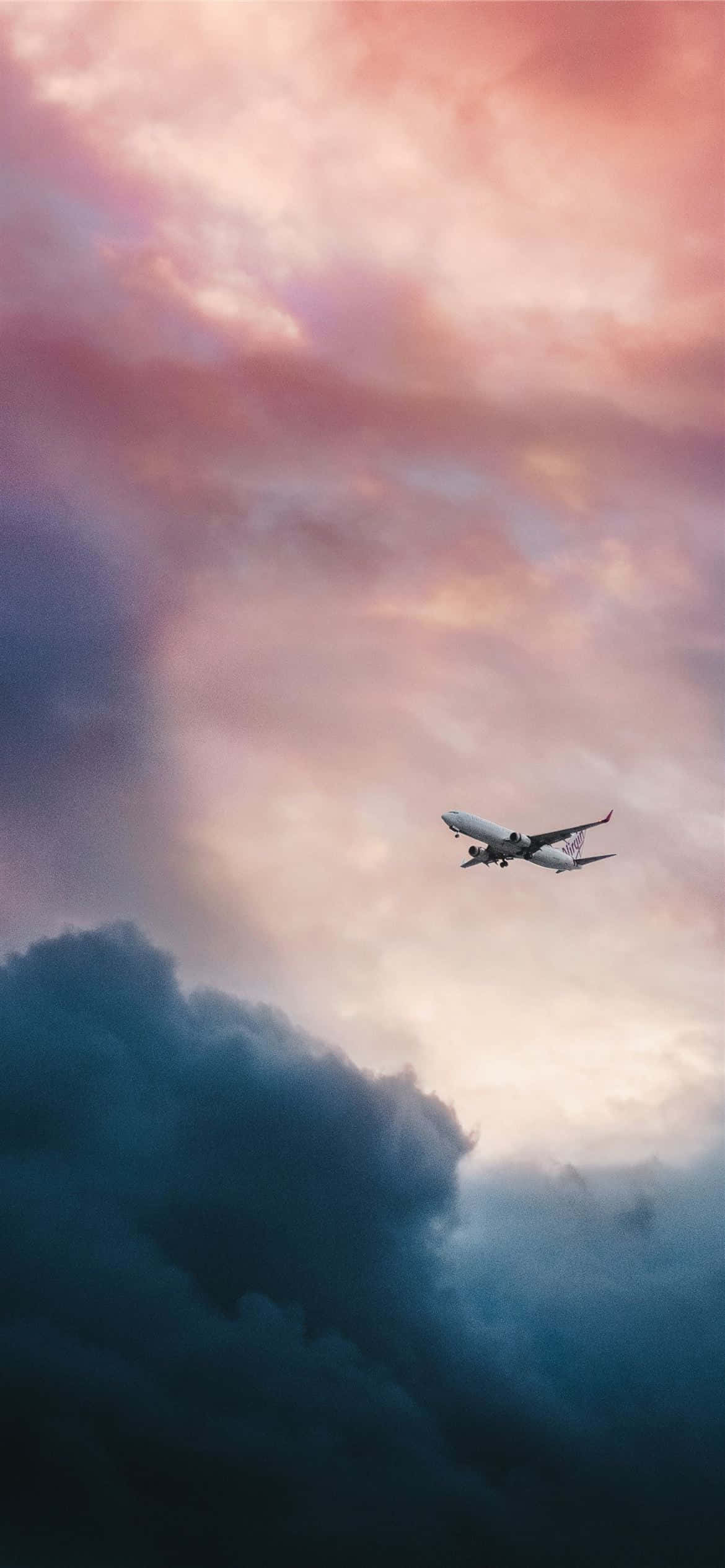 Plane 桌布 壁紙 — 一架孤獨的飛機在暮色中翱翔，穿越由粉紅、橙色和深藍色雲彩繪成的戲劇性天空。