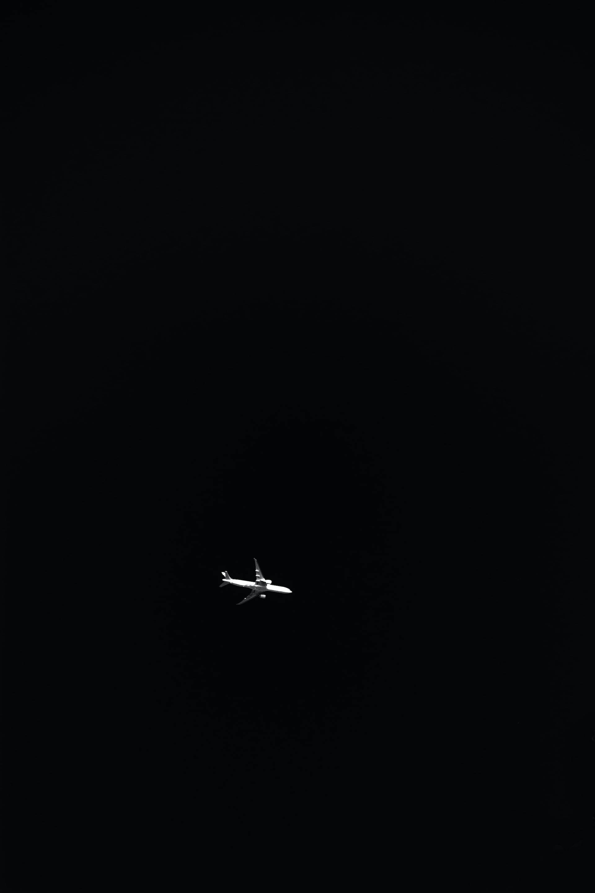飛機 桌布 壁紙 — 一架孤獨的飛機在漆黑的天空中滑翔，其輪廓在虛空中顯得格外鮮明。