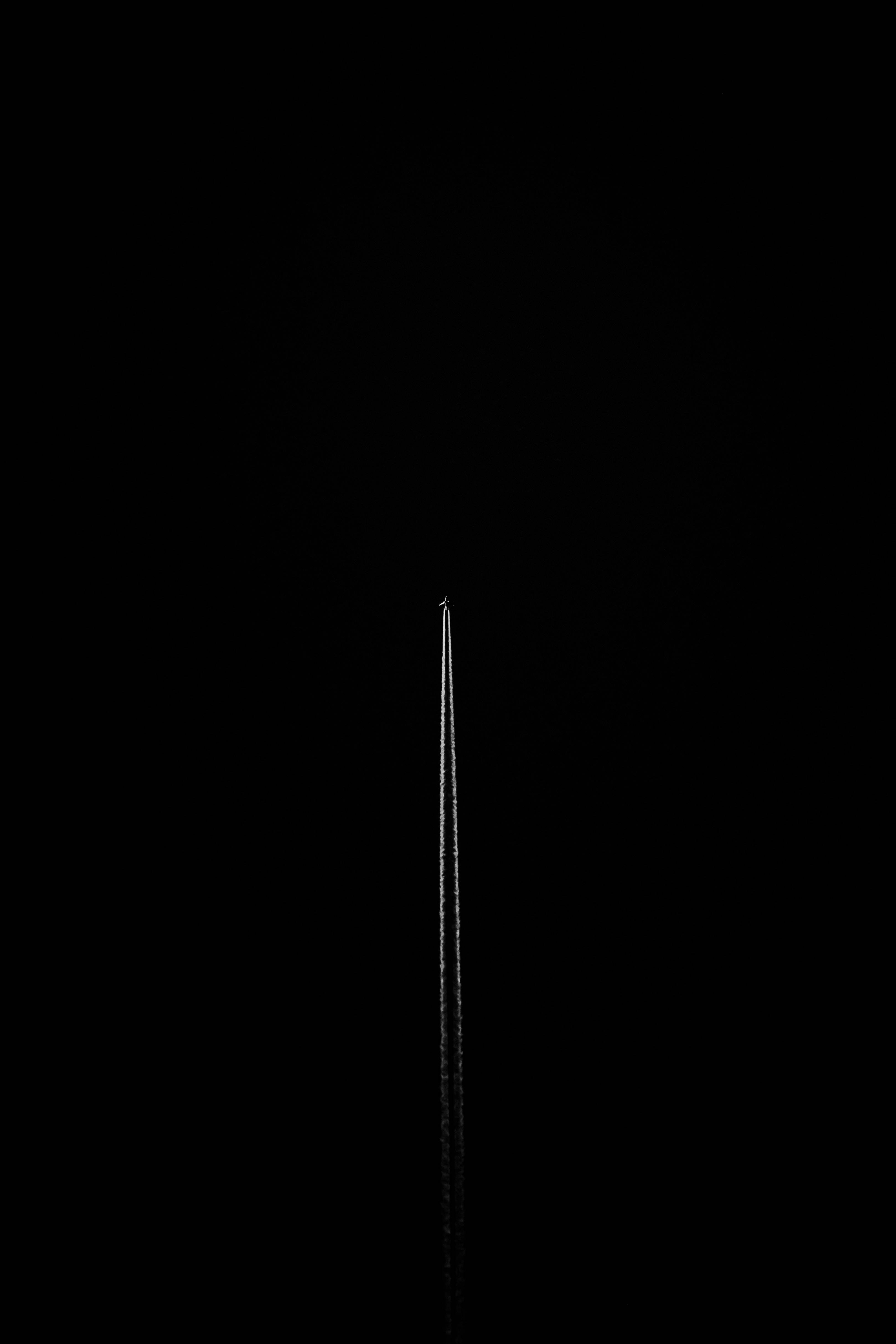 jet iPhone 桌布 壁紙 — 一架孤獨的飛機在無盡的黑色天空中留下一道明亮的凝結尾跡。