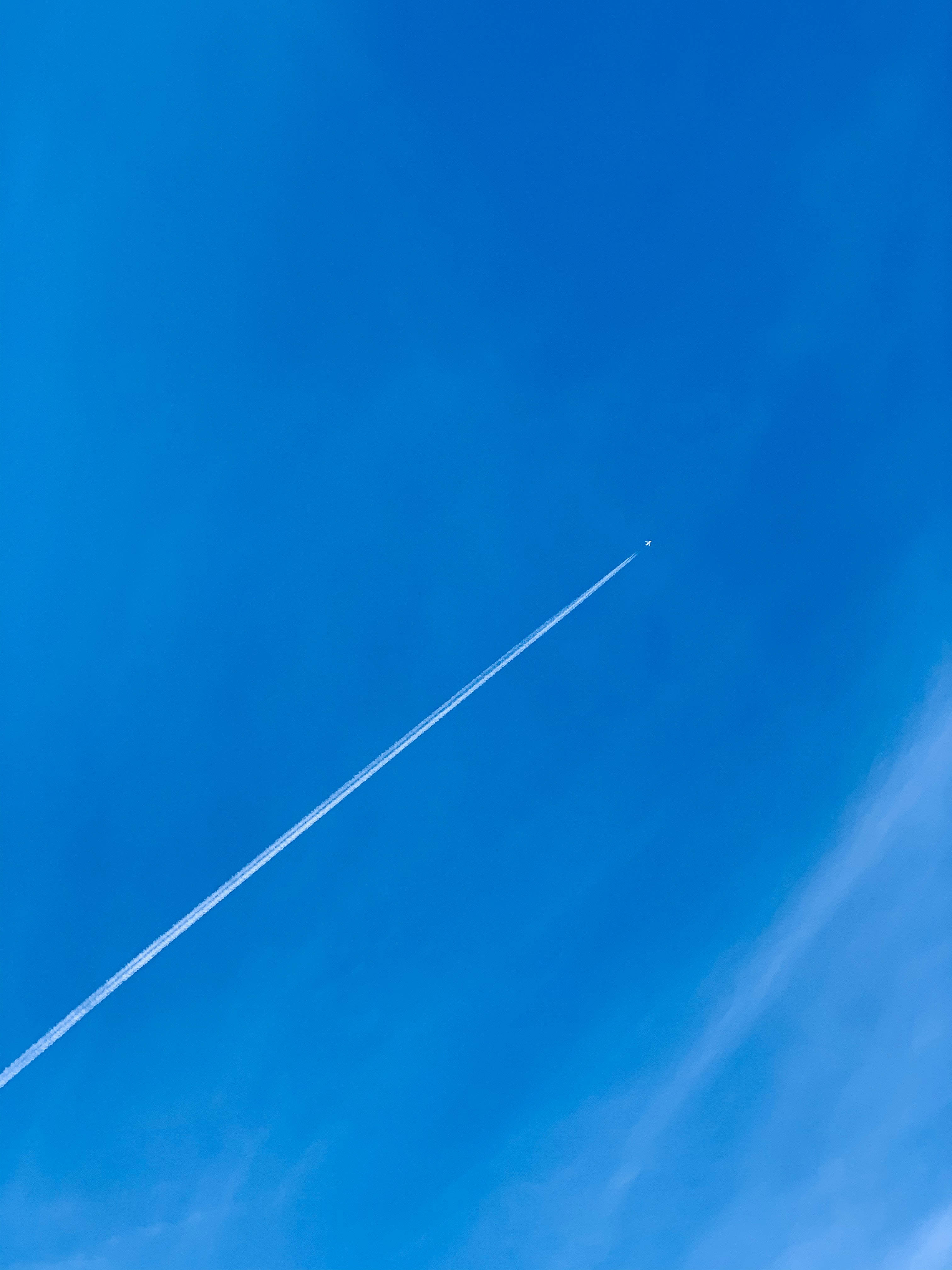 飛機 桌布 壁紙 — 一架孤獨的飛機留下一道清晰的白色凝結尾跡，斜斜地劃過廣闊無雲的蔚藍天空。
