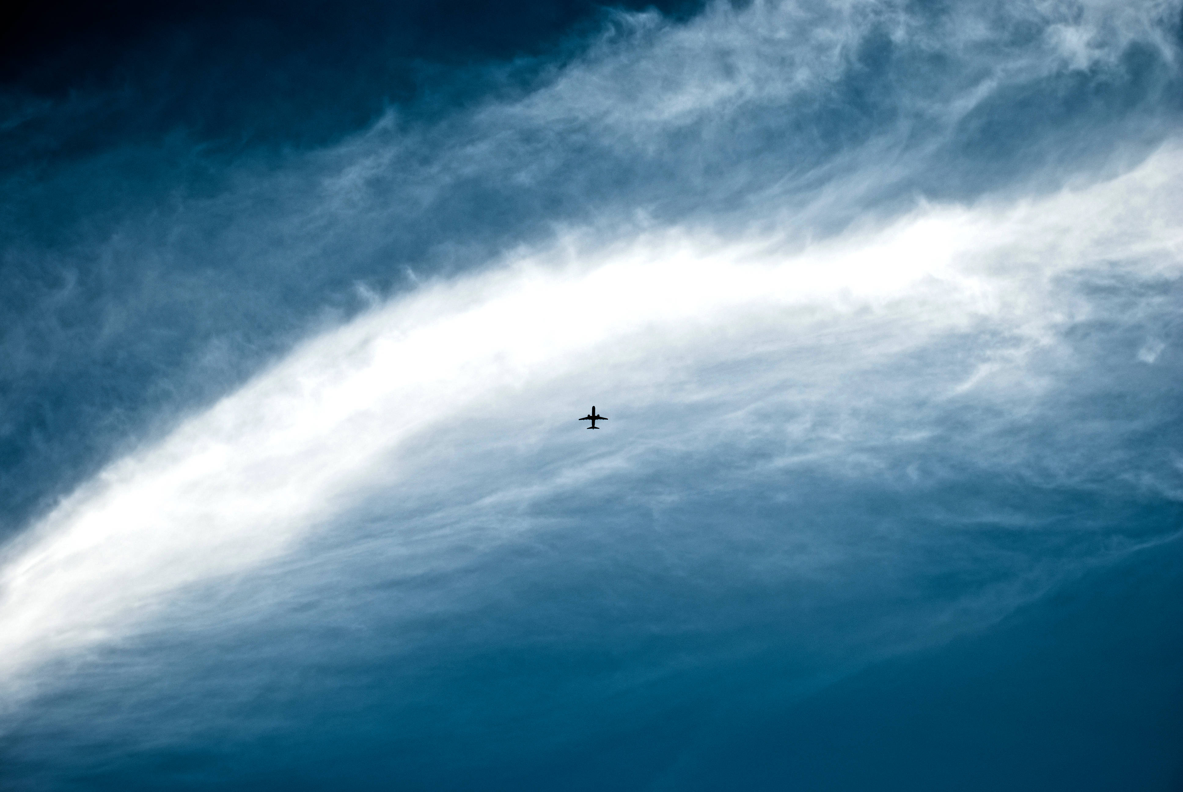 Plane 桌布 壁紙 — 一架孤獨的飛機飛過戲劇性的天空，明亮的白色雲彩襯托著深藍色。