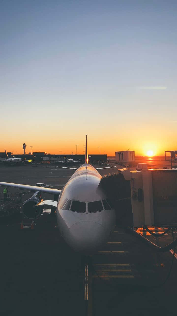 日落 桌布 壁紙 — 一架客機停靠在機場閘口，夕陽在橙色和藍色的漸變天空中落下。