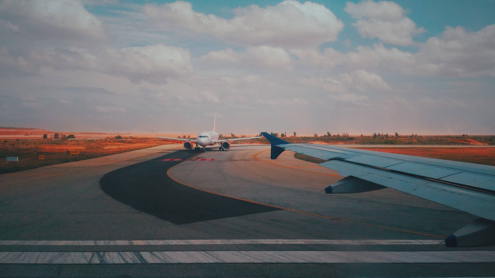 Runway 桌布 壁紙 — 一架客機在多雲的天空下，沿著彎曲的跑道滑行，帶有溫暖的日落色調。