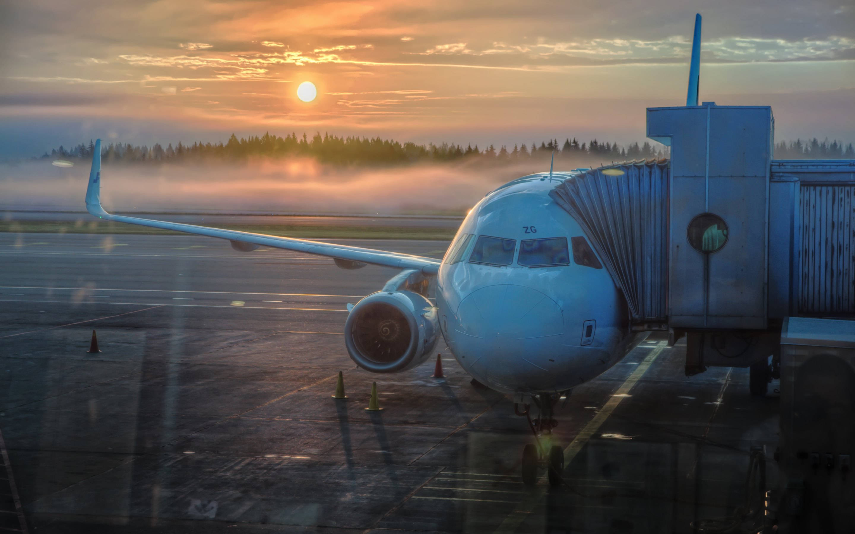 Airport 桌布 壁紙 — 一架客機在霧氣瀰漫的日出時分停靠在登機閘口，金色的陽光在濕漉漉的停機坪上投下長長的影子。