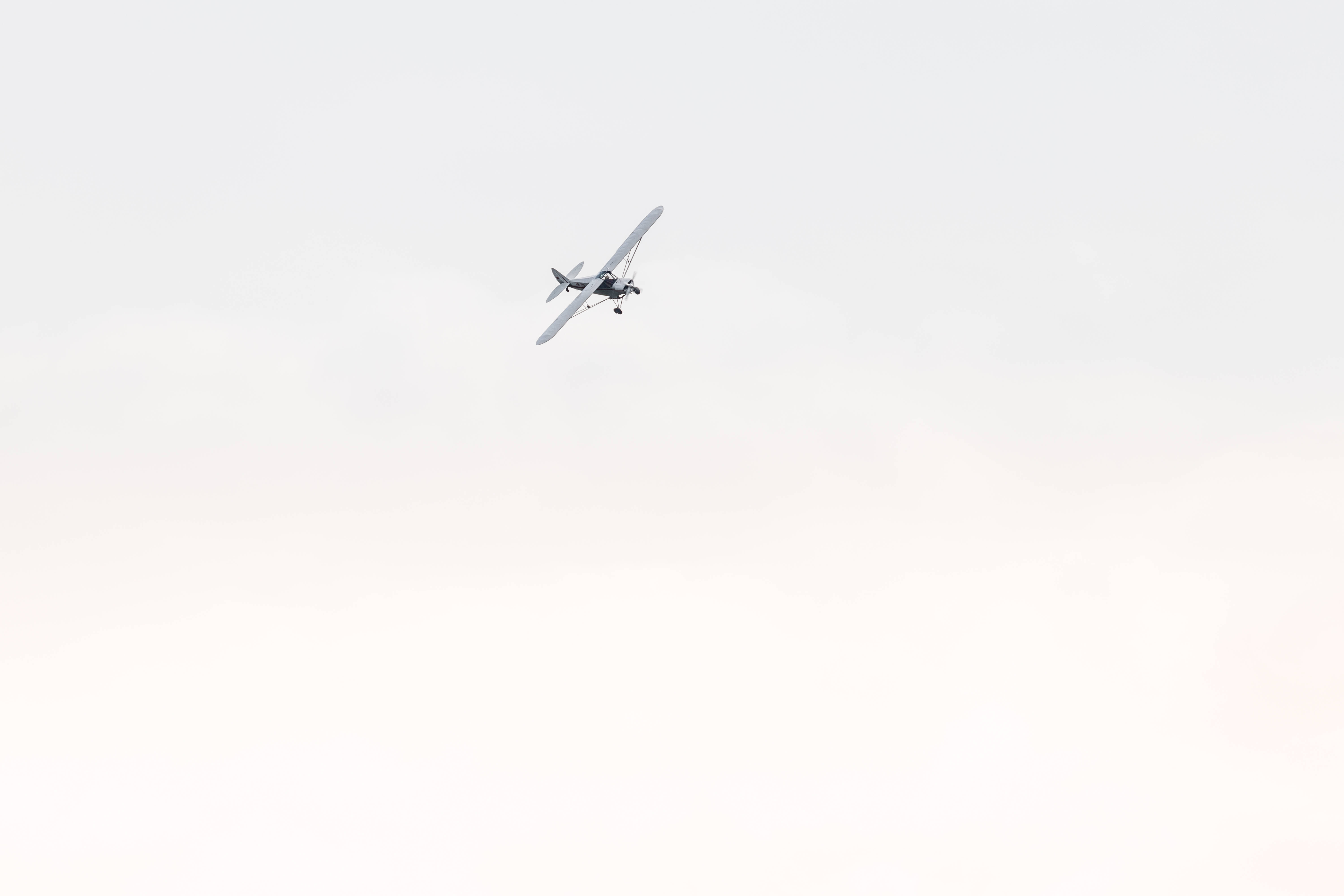 small 桌布 壁紙 — 一架小型單引擎飛機獨自翱翔在廣闊蒼白、雲層柔軟的天空中。