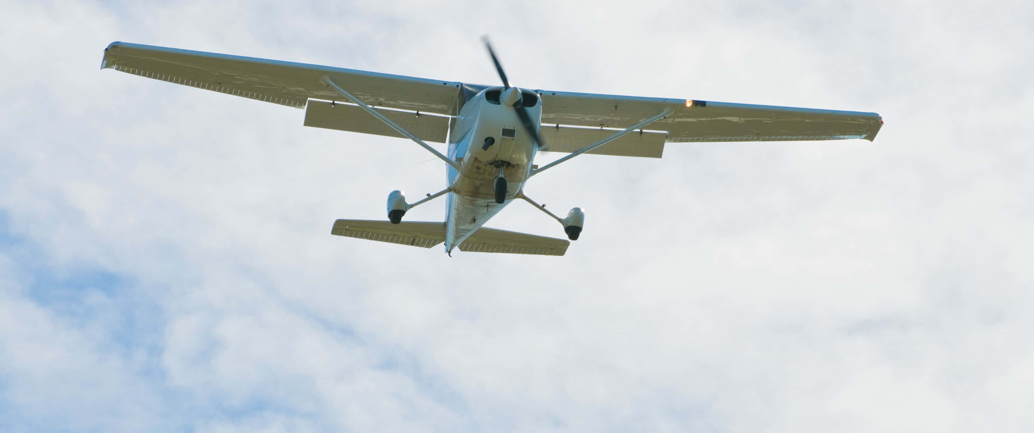 3440x1440p Small Planes 桌布 壁紙 — 一架小型白色單引擎飛機在部分多雲的藍天中飛過頭頂。
