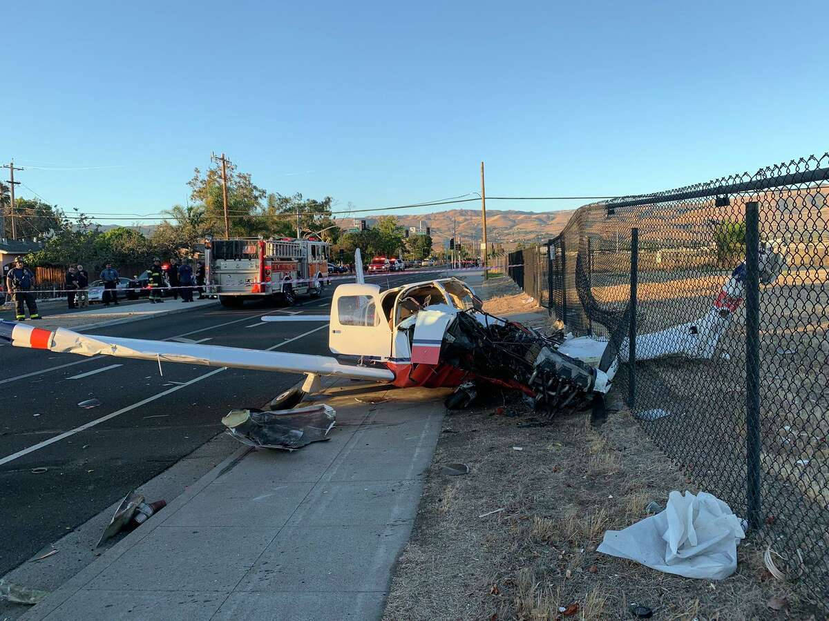 plane crash 桌布 壁紙 — 一架小型飛機在路邊圍籬旁墜毀，緊急救援人員和消防車在晴朗藍天下應對。