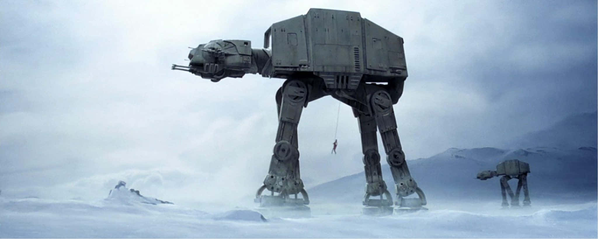 At-at 桌布 壁紙 — 一架巨大的AT-AT步行機在雪地戰場上大步前行，一個細小的人影掛在其腿部，背景是陰雲密佈的天空。