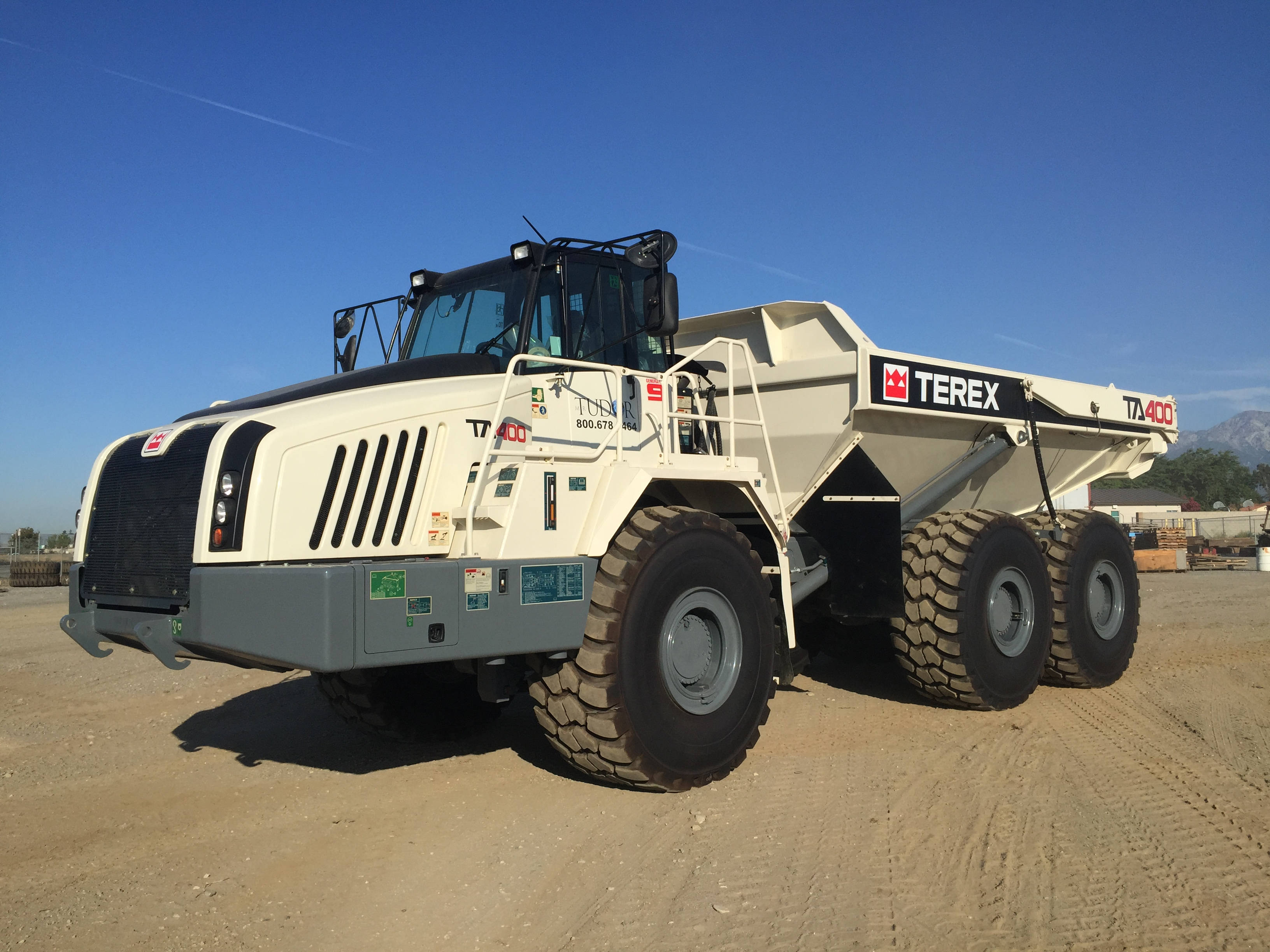 Cool Truck 桌布 壁紙 — 一架巨大的白色Terex TA400傾卸車停在塵土飛揚的地形上，背景是晴朗的藍天和遠山。