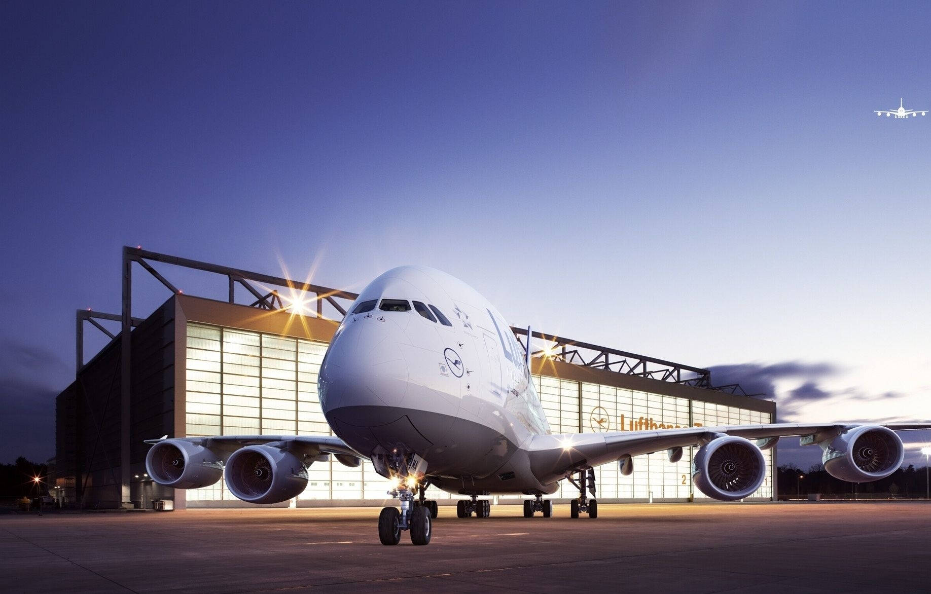 飛機 桌布 壁紙 — 一架巨大的白色漢莎航空空中巴士A380在黃昏時分停在機場停機坪上，背後是發光的機庫。