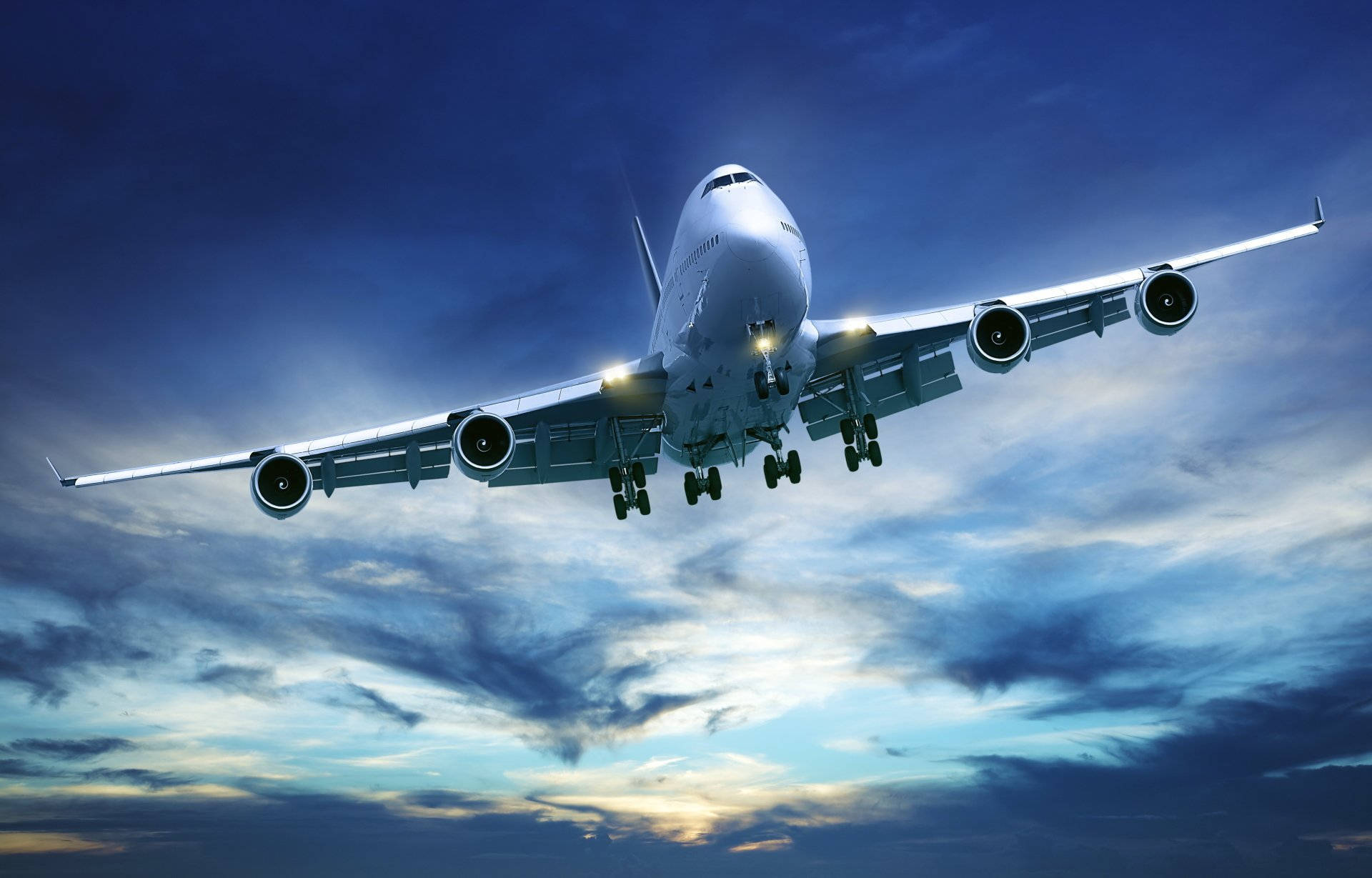 flying 桌布 壁紙 — 一架巨大的白色珍寶客機放下起落架，在佈滿藍色和金色雲彩的戲劇性暮色天空中下降。