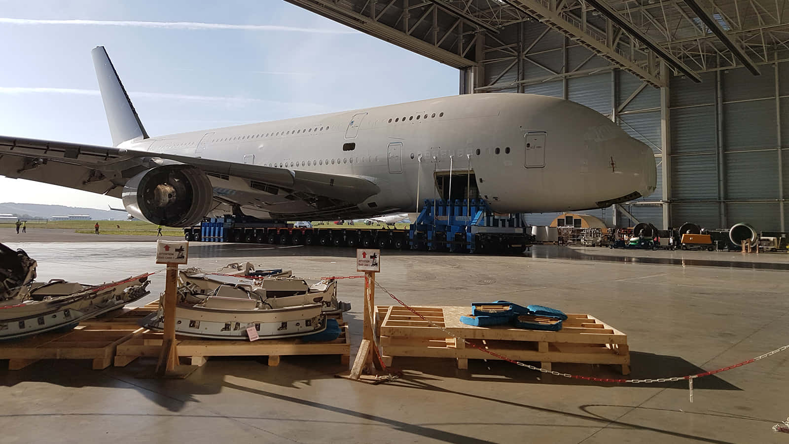 桌布 壁紙 — 一架巨大的白色空中巴士A380停放在機庫內的混凝土地面上，附近木製棧板上有小船。