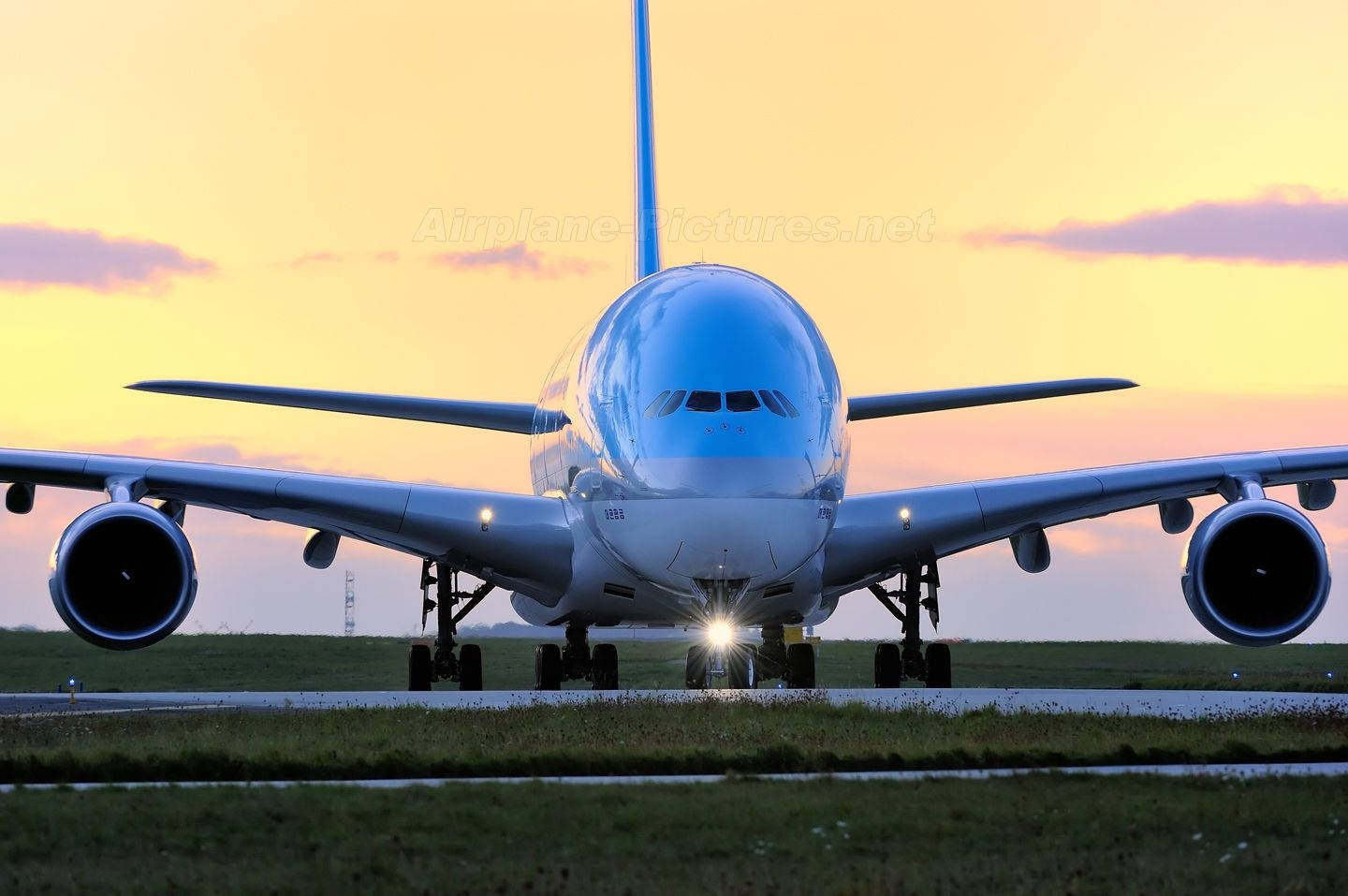  壁紙 — 一架巨大的白色空中巴士A380飛機在日落時分停在跑道上，背後有發光的燈光和金色的天空。