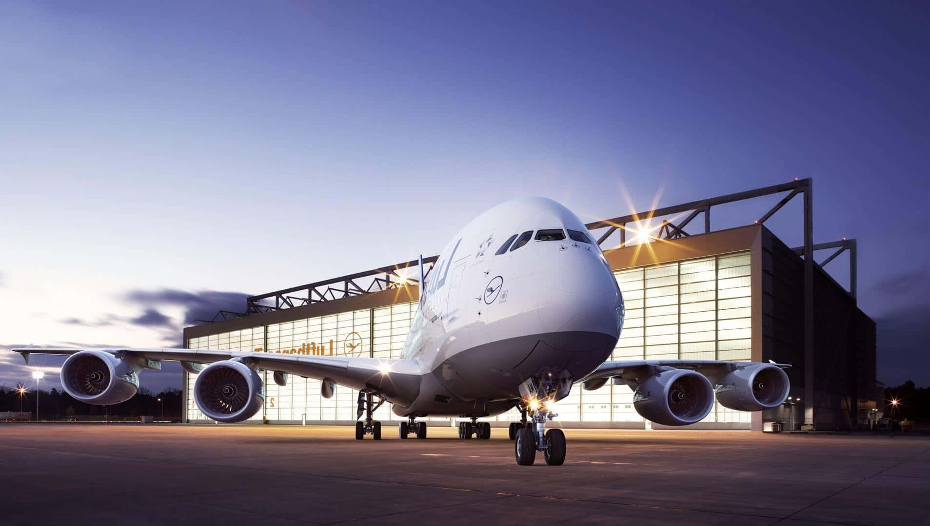 機場 桌布 壁紙 — 一架巨大的白色空中巴士A380飛機在黃昏時停在機場停機坪上，後面有一個發光的機庫。