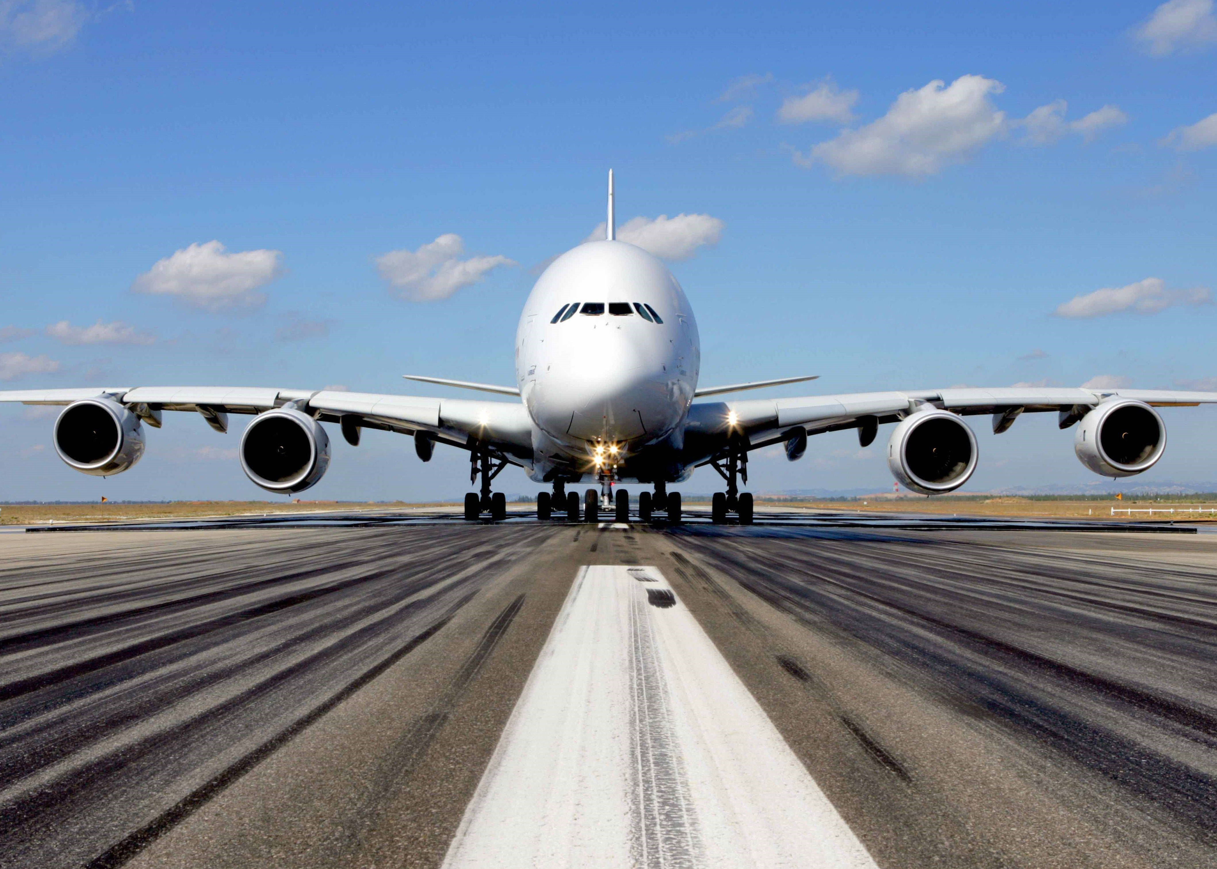 4K 飛機壁紙 桌布 壁紙 — 一架巨大的白色空中巴士A380飛機在晴朗藍天和零星雲朵下，正面接近跑道。